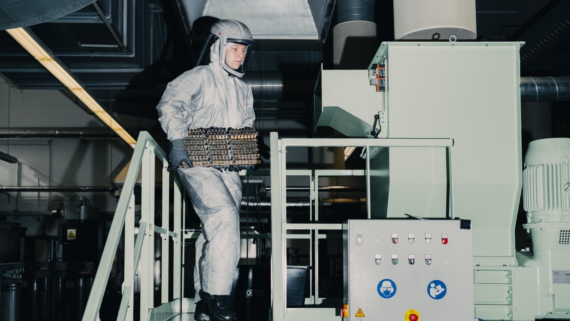 Worker in protective suit carrying battery cells to a shredder for recycling