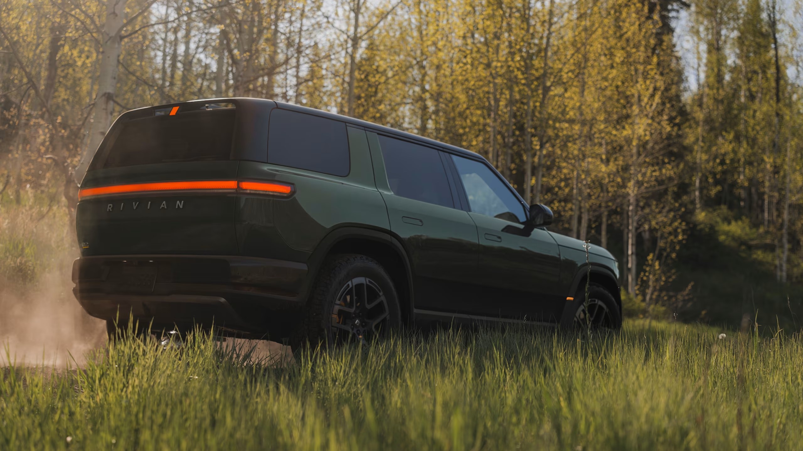 Rivian R2 in Forest Green paint, rear three-quarter view in a forest