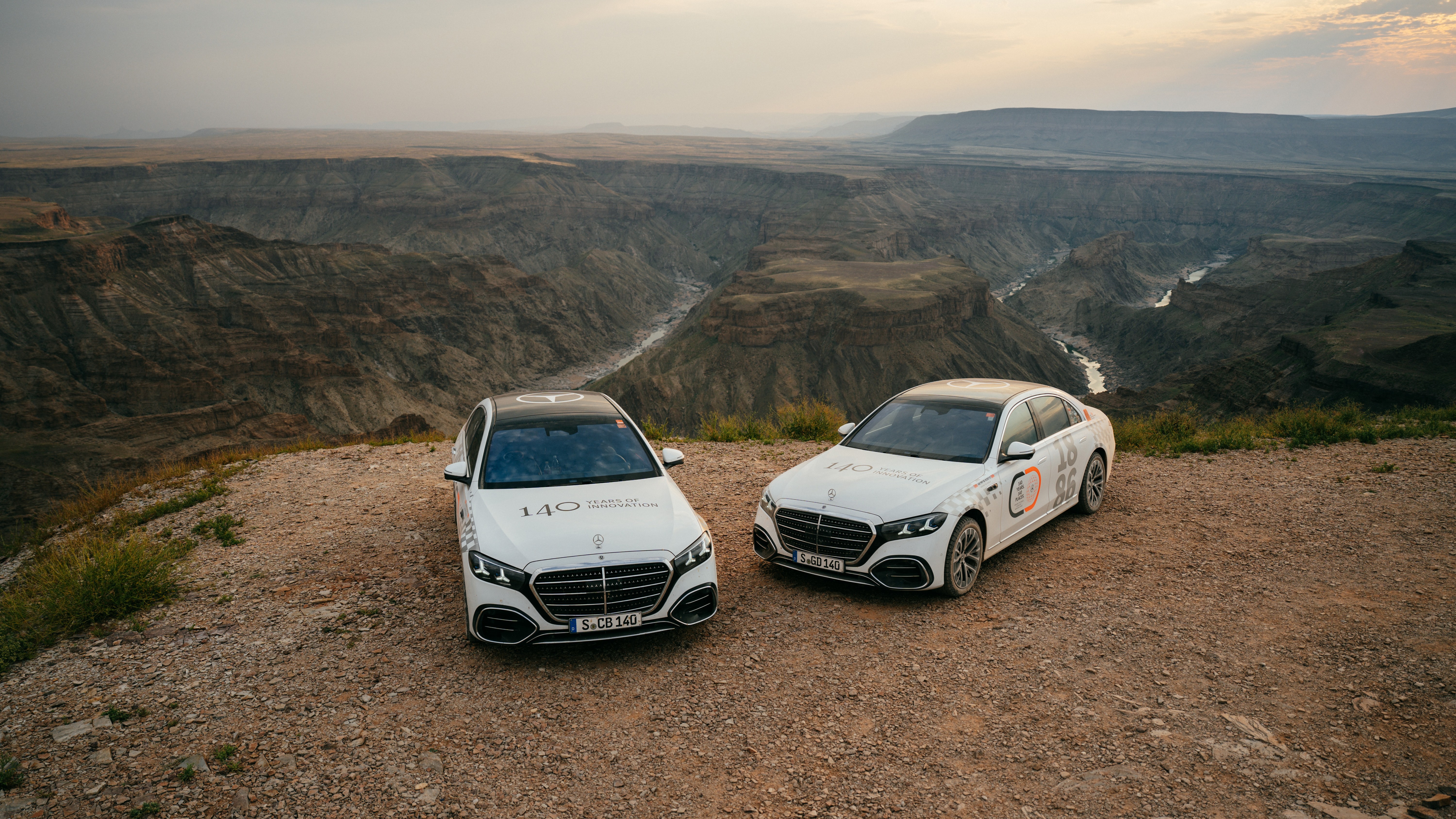Two Mercedes S-Class sedans parked at a desert canyon overlook in Africa