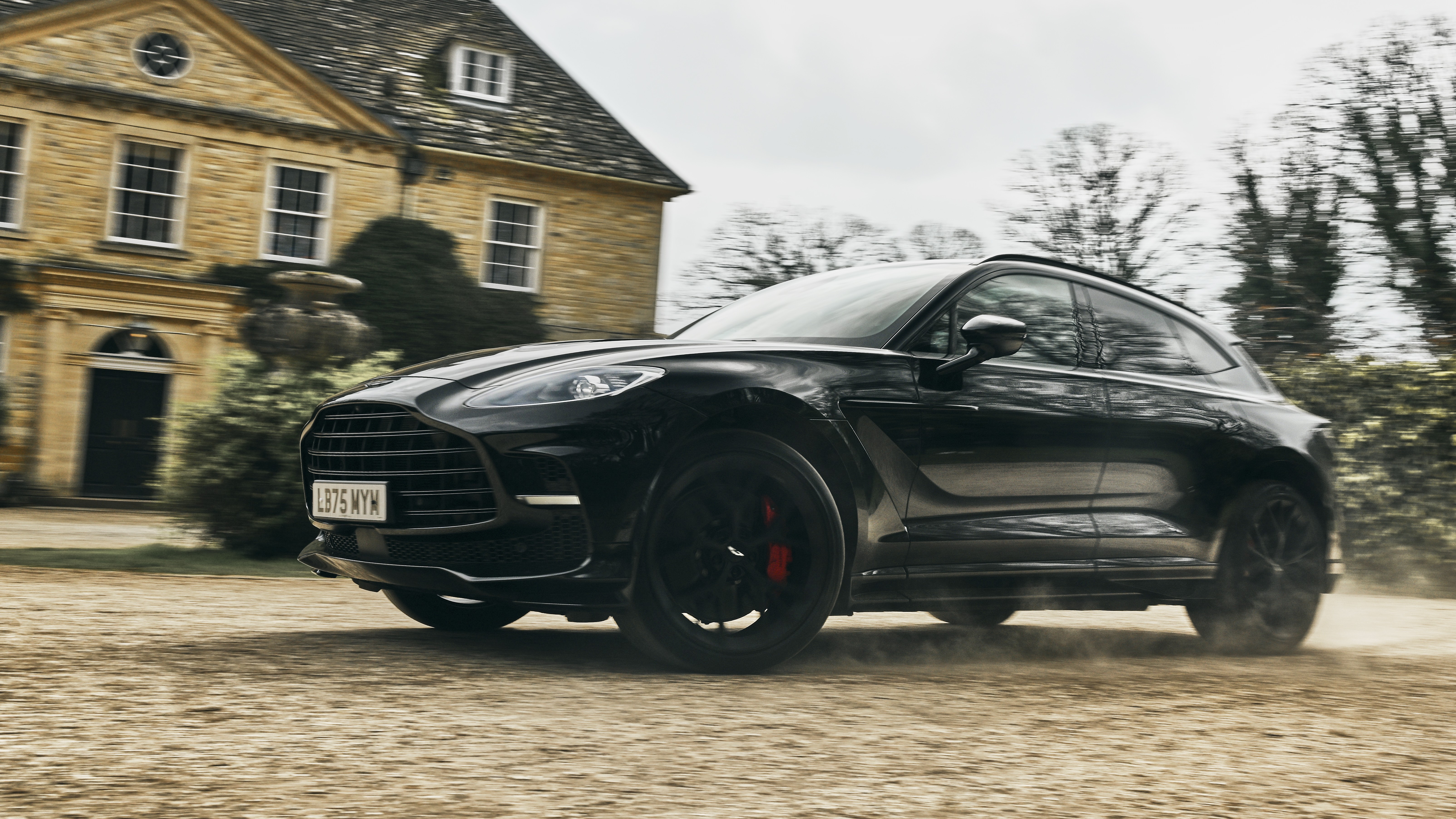 Black Aston Martin DBX driving on gravel outside a country estate