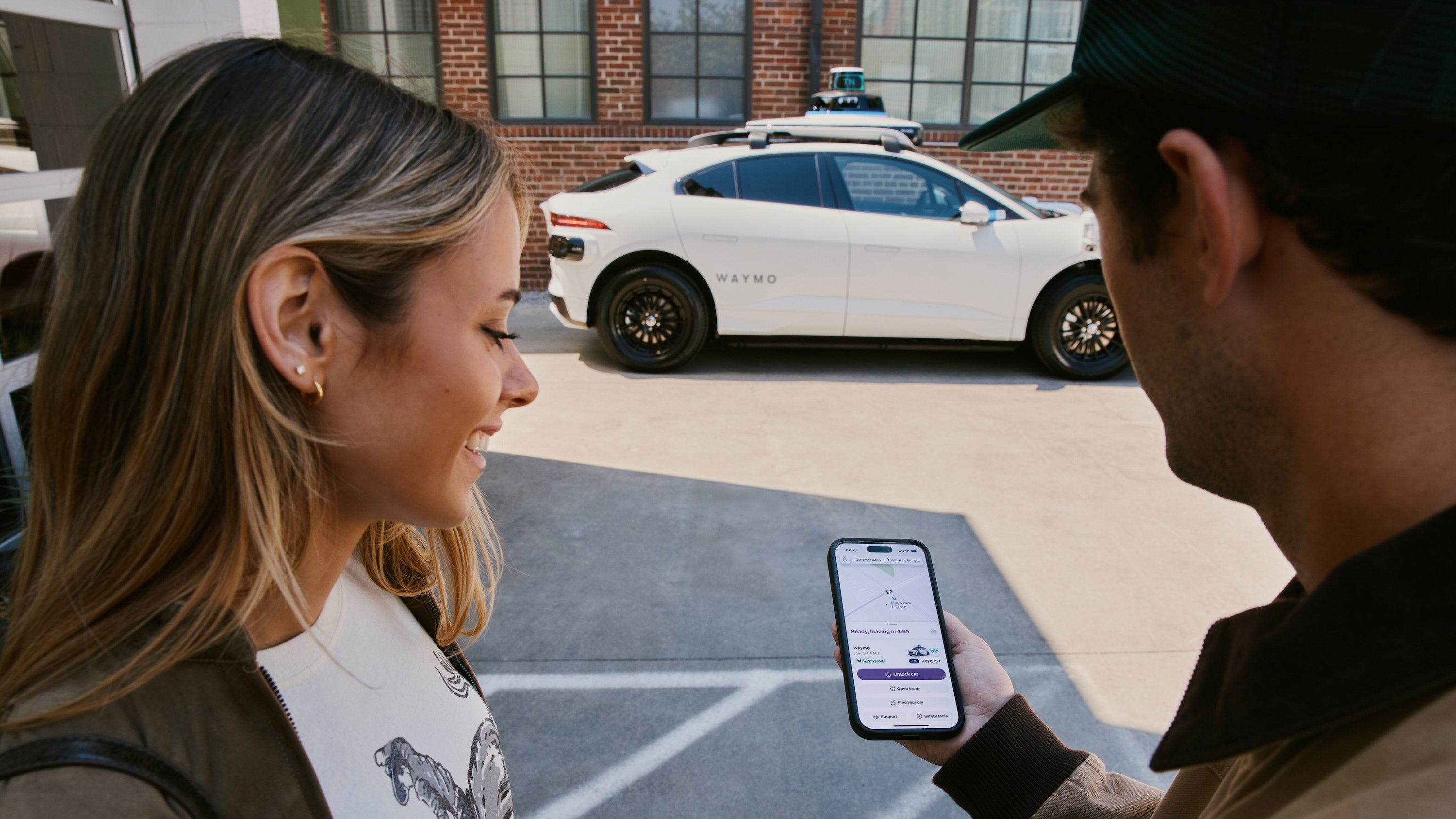Riders check the Lyft app next to a Waymo Jaguar I-Pace in Nashville