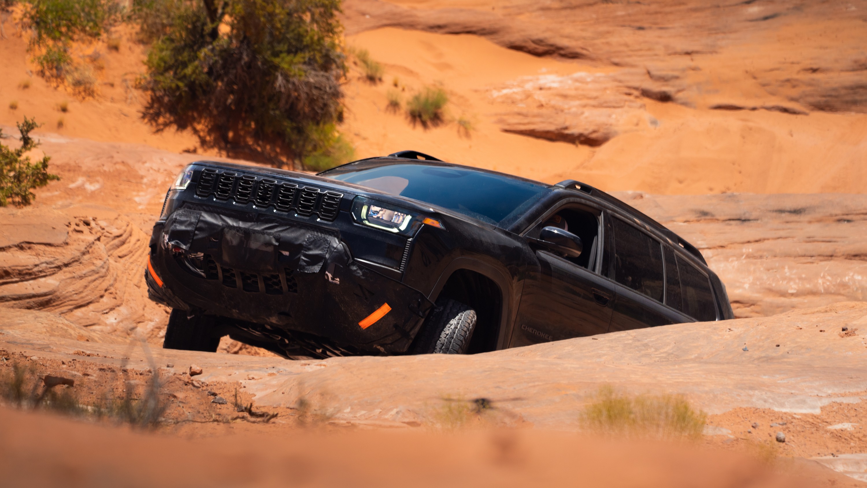 Camouflaged Jeep Cherokee Trailhawk prototype crawling through a slickrock channel