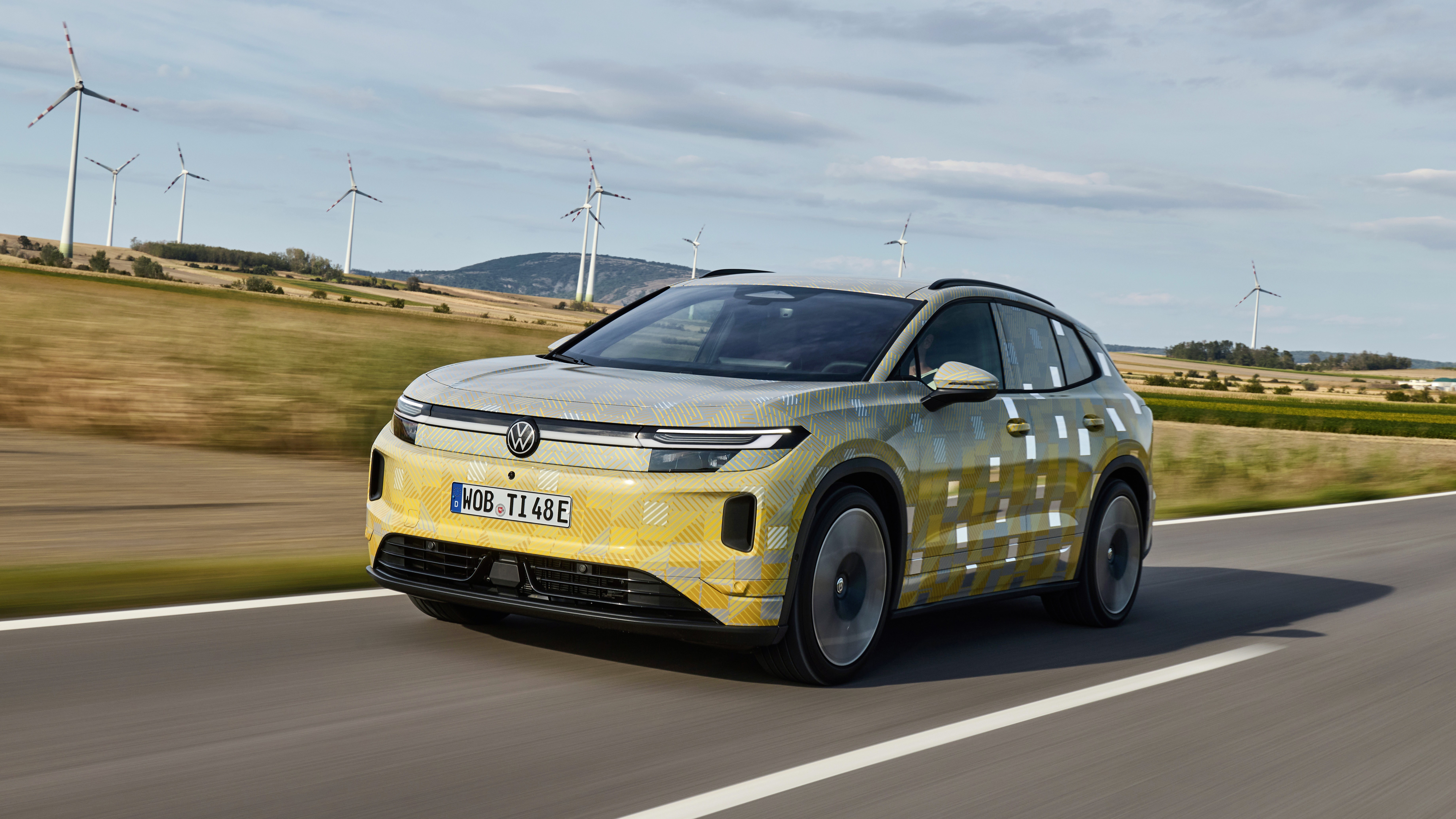 Camouflaged Volkswagen ID. Tiguan prototype driving past wind turbines