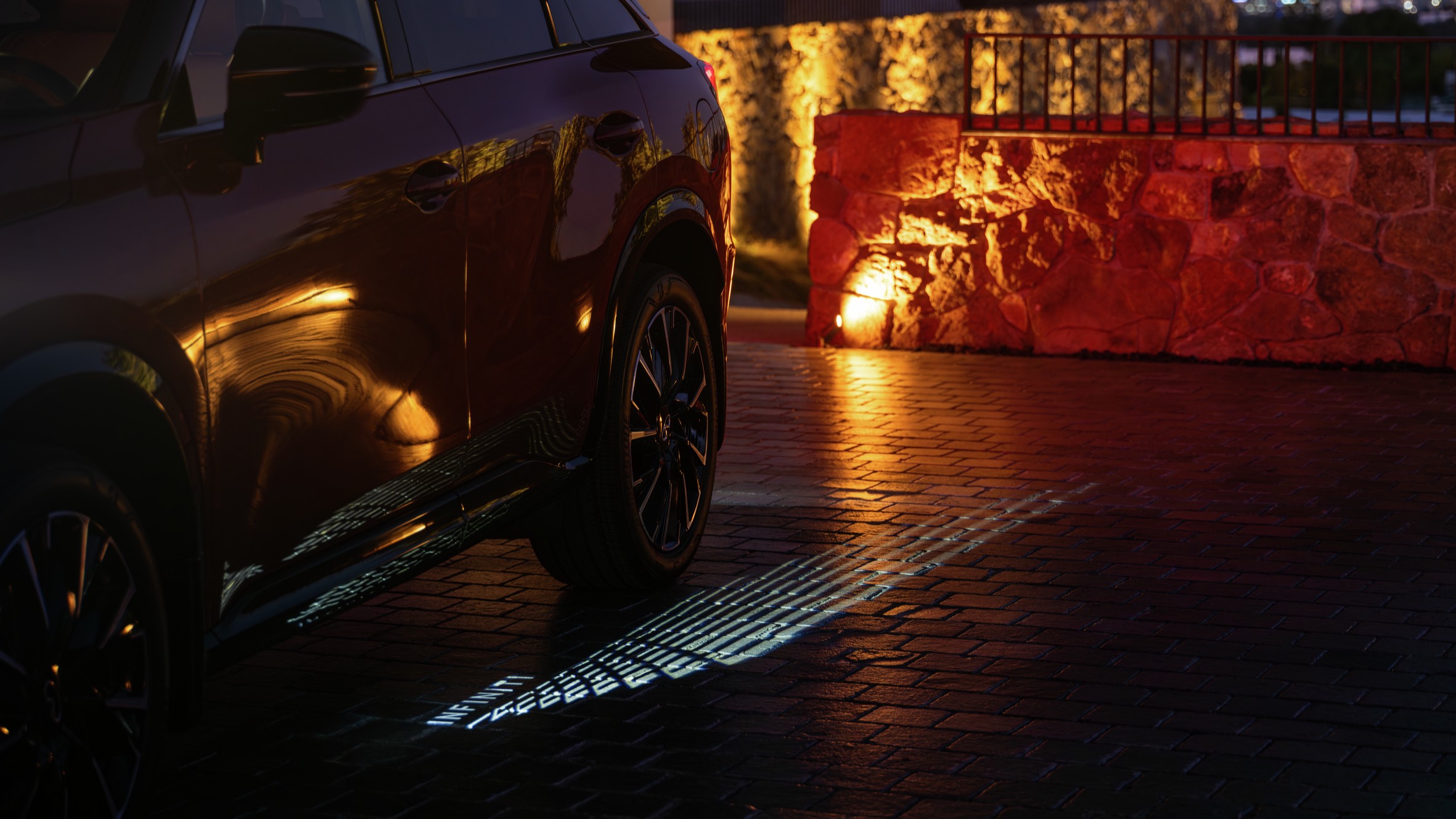 Infiniti QX65 projecting Light Path pattern and wordmark onto pavement at dusk