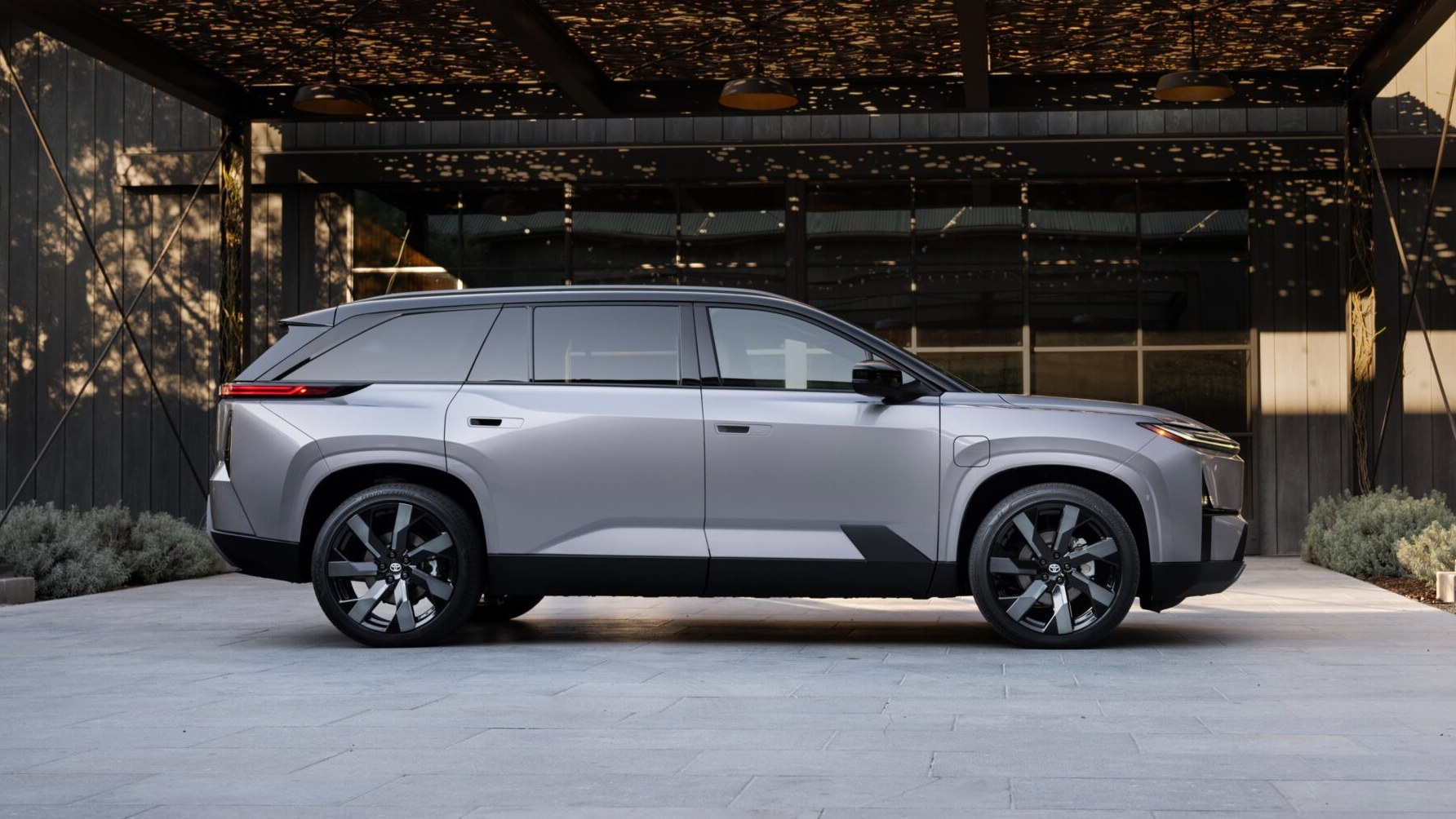 Silver 2028 Toyota Highlander electric SUV in profile outside a modern building