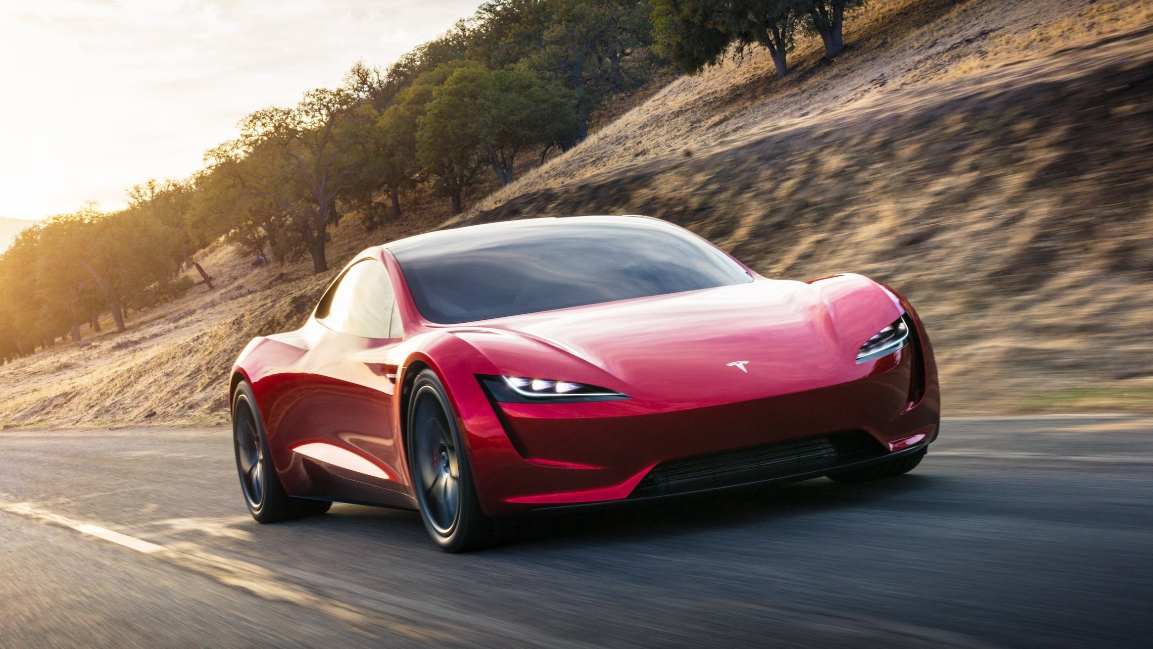 Red 2017 Tesla Roadster prototype driving on a hillside road at sunset