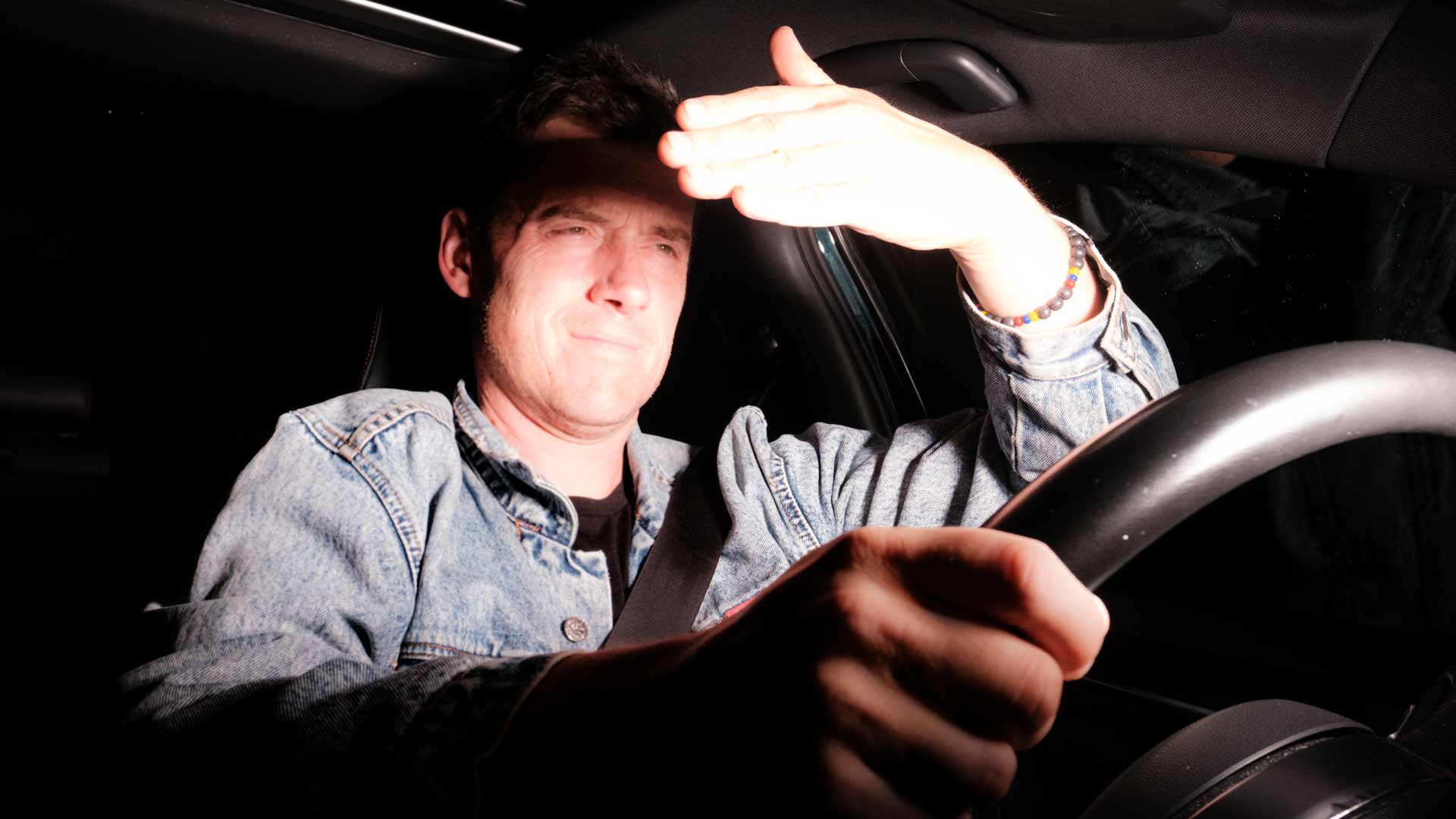 Driver shields his eyes from oncoming headlight glare at night