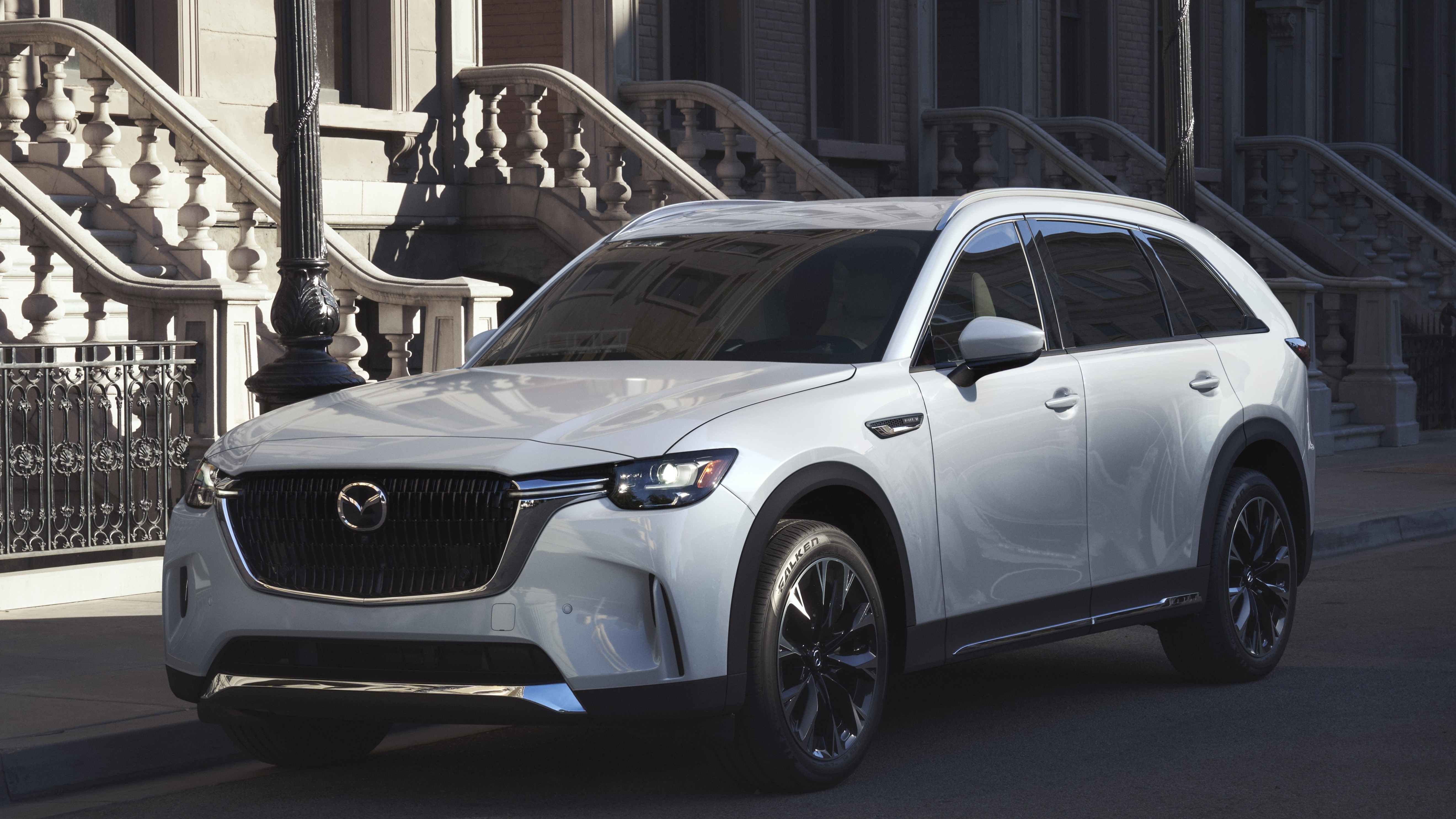White Mazda CX-90 three-row SUV parked on a city street, front three-quarter view