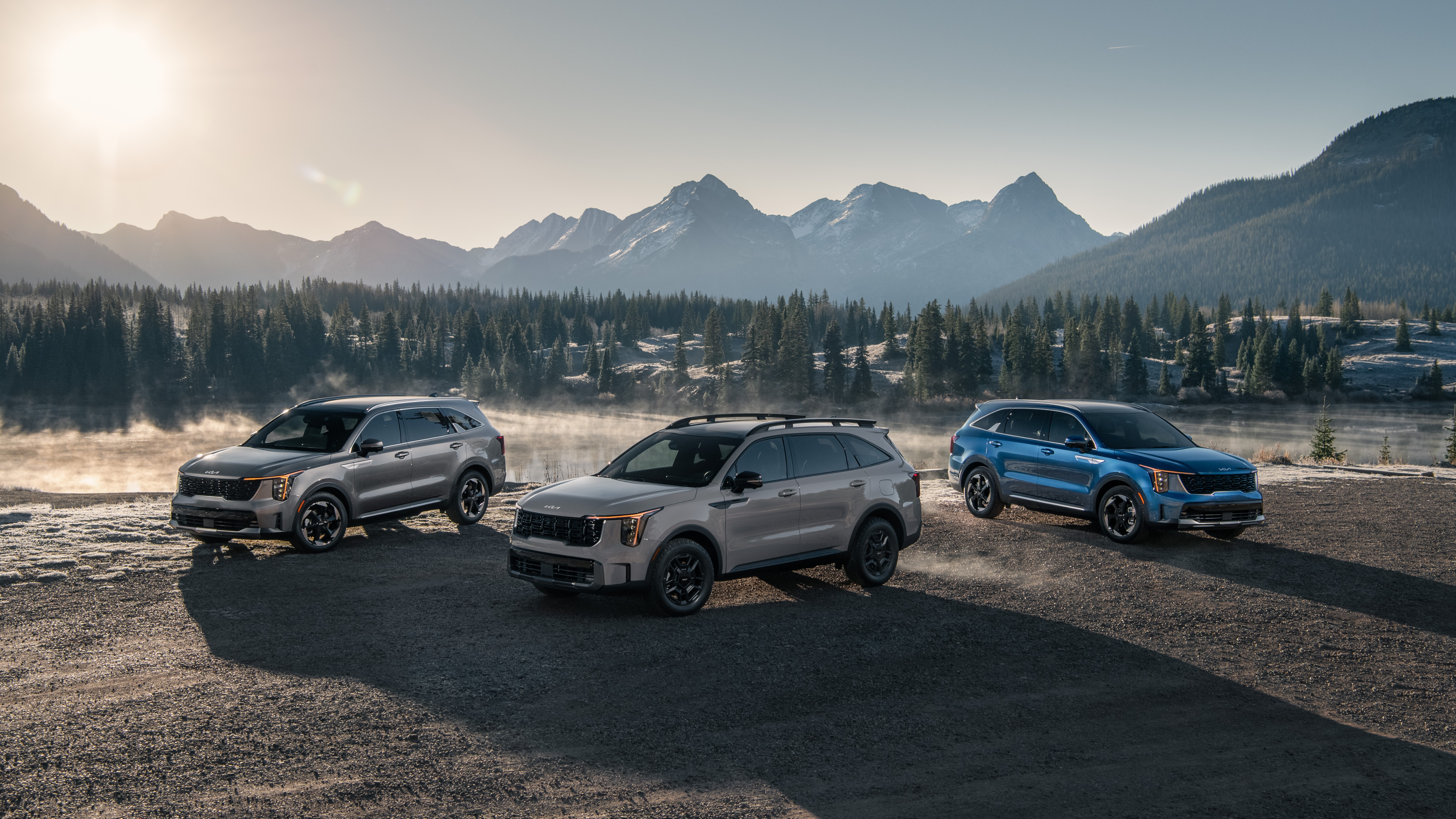 Three 2027 Kia Sorento SUVs parked by a mountain lake