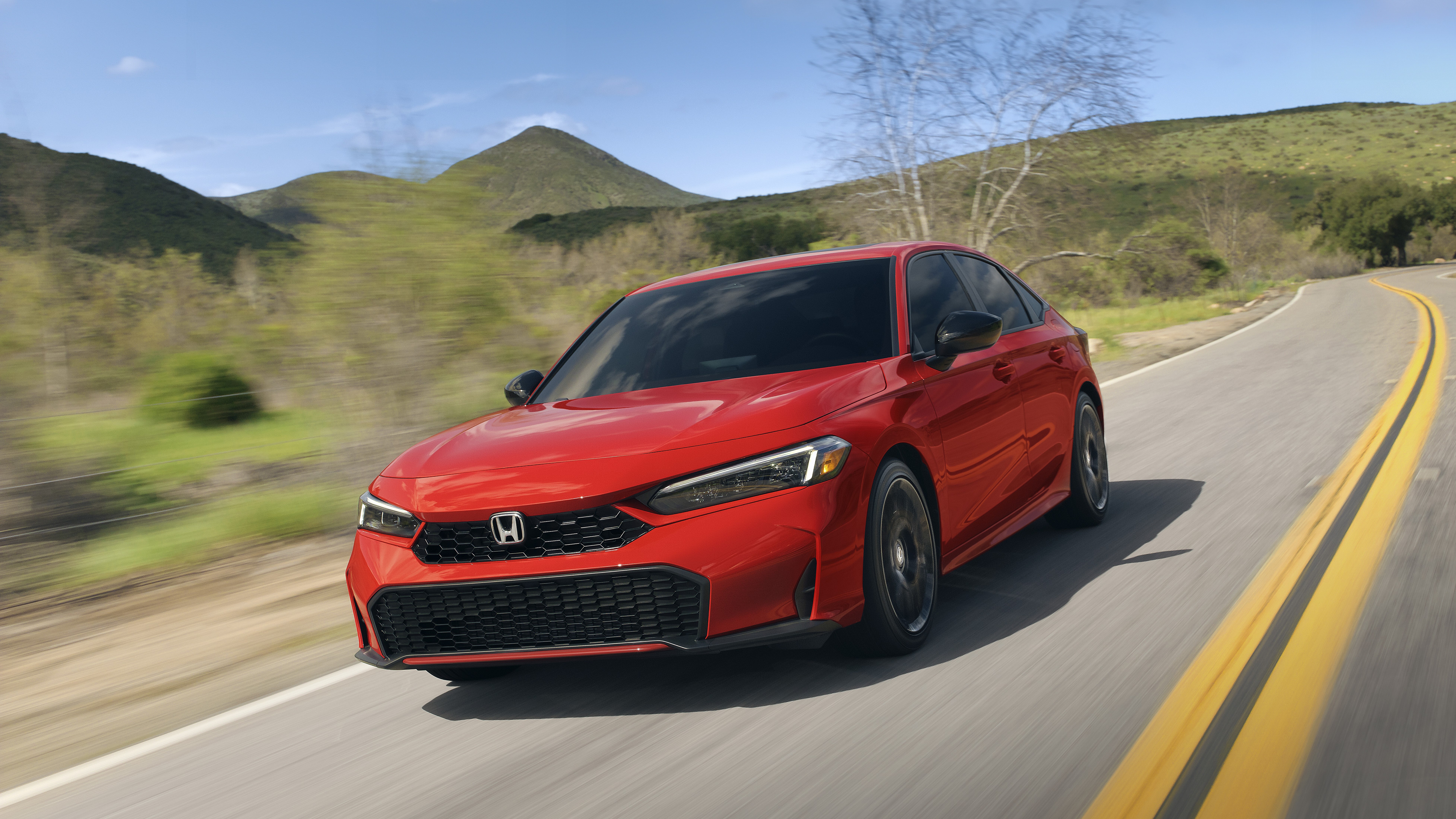 Red 2027 Honda Civic sedan driving on a winding road, front three-quarter view