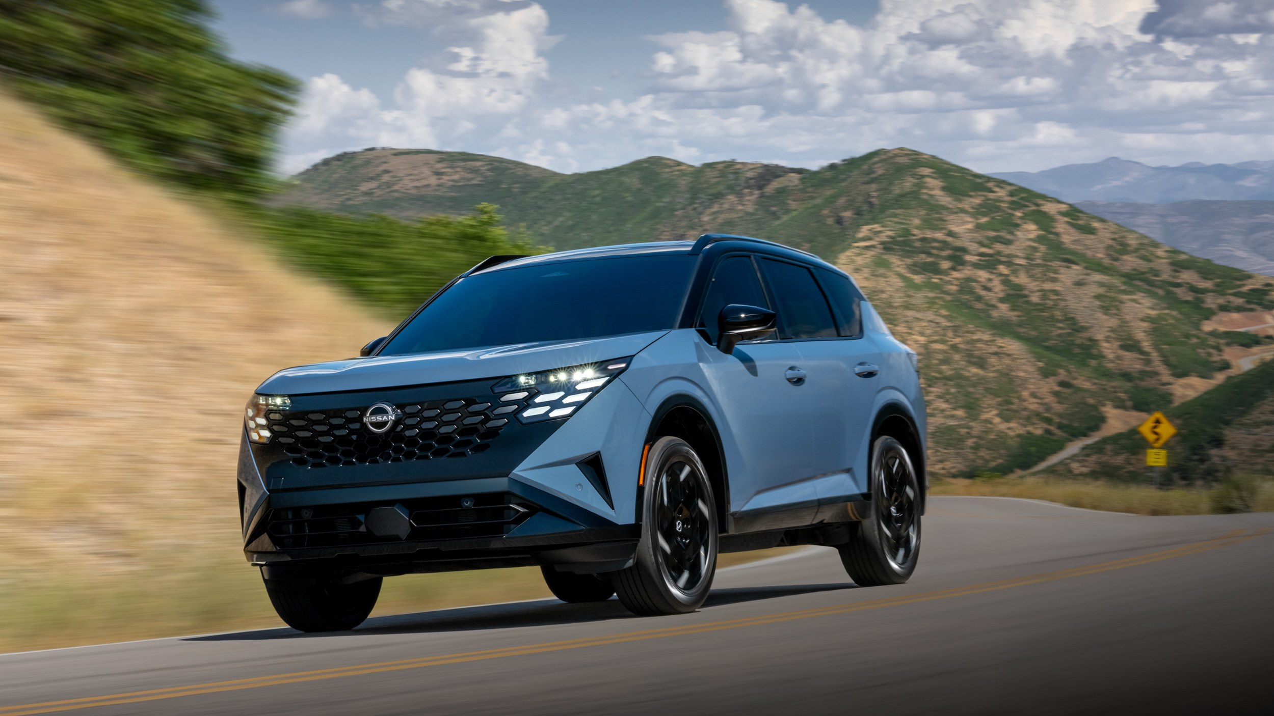 2027 Nissan Rogue Hybrid SR driving on a mountain road, front three-quarter view