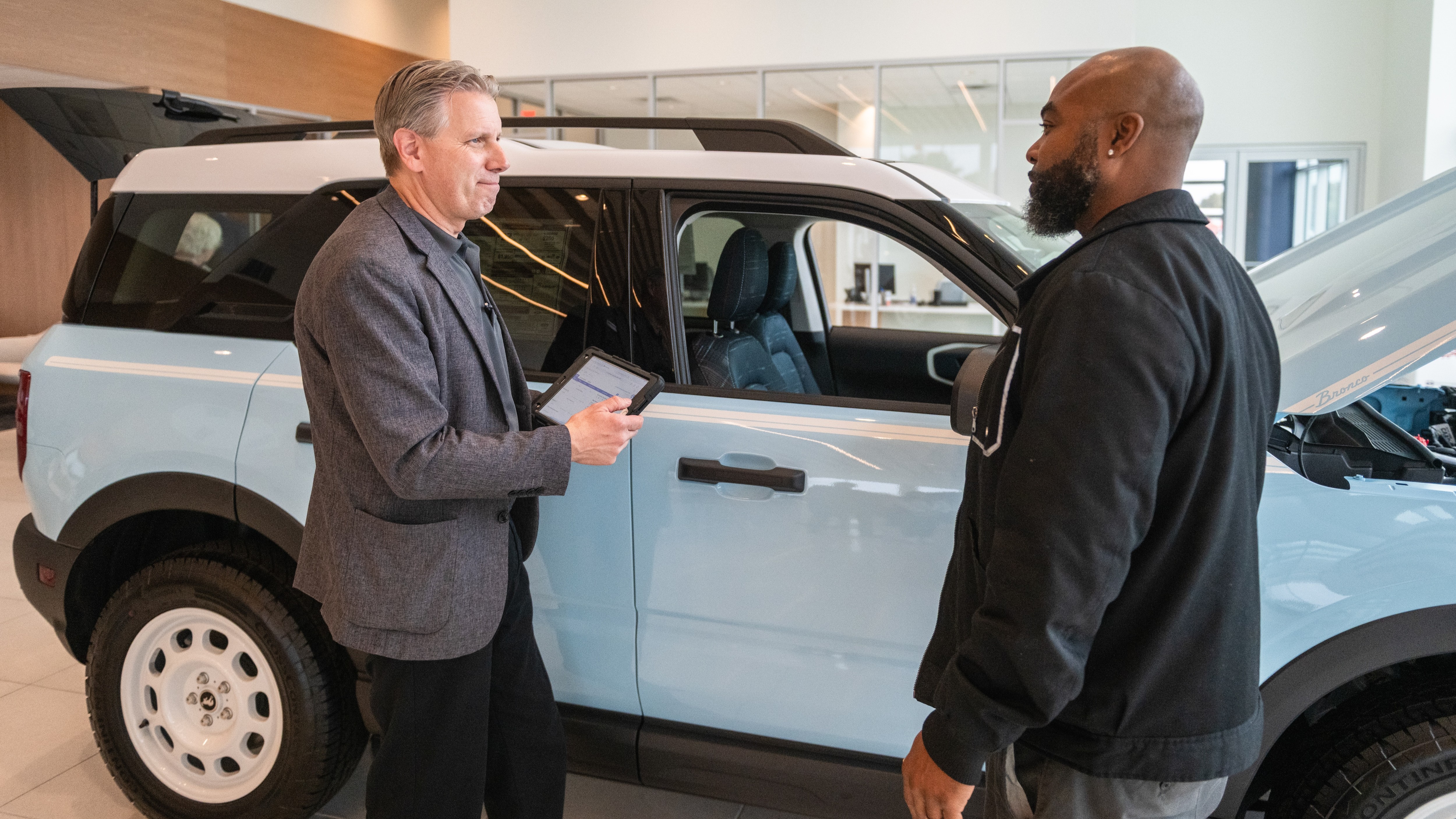 Two men talk beside a vehicle inside a Ford dealership
