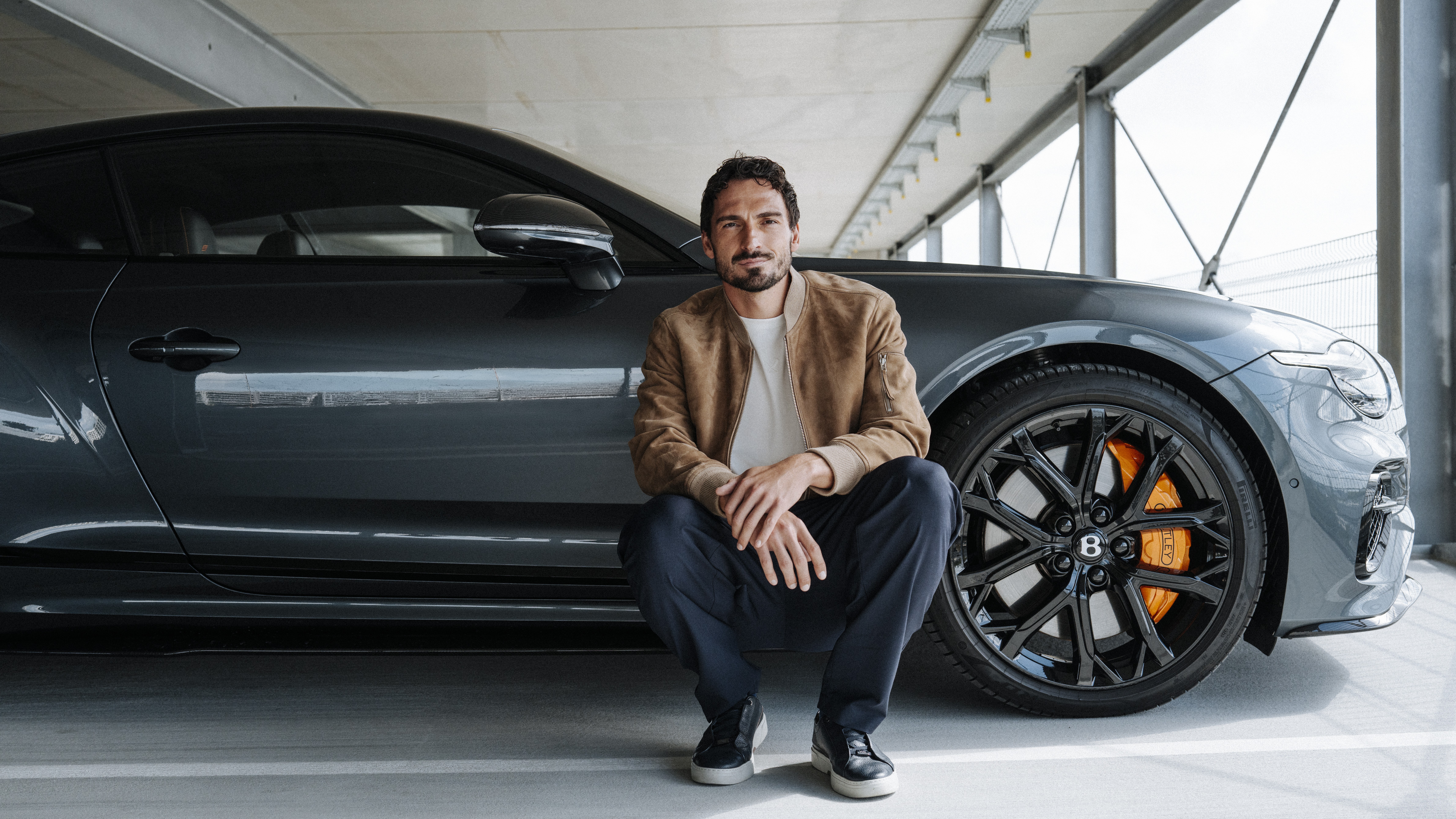 Mats Hummels crouching beside a gray Bentley Continental GT Speed