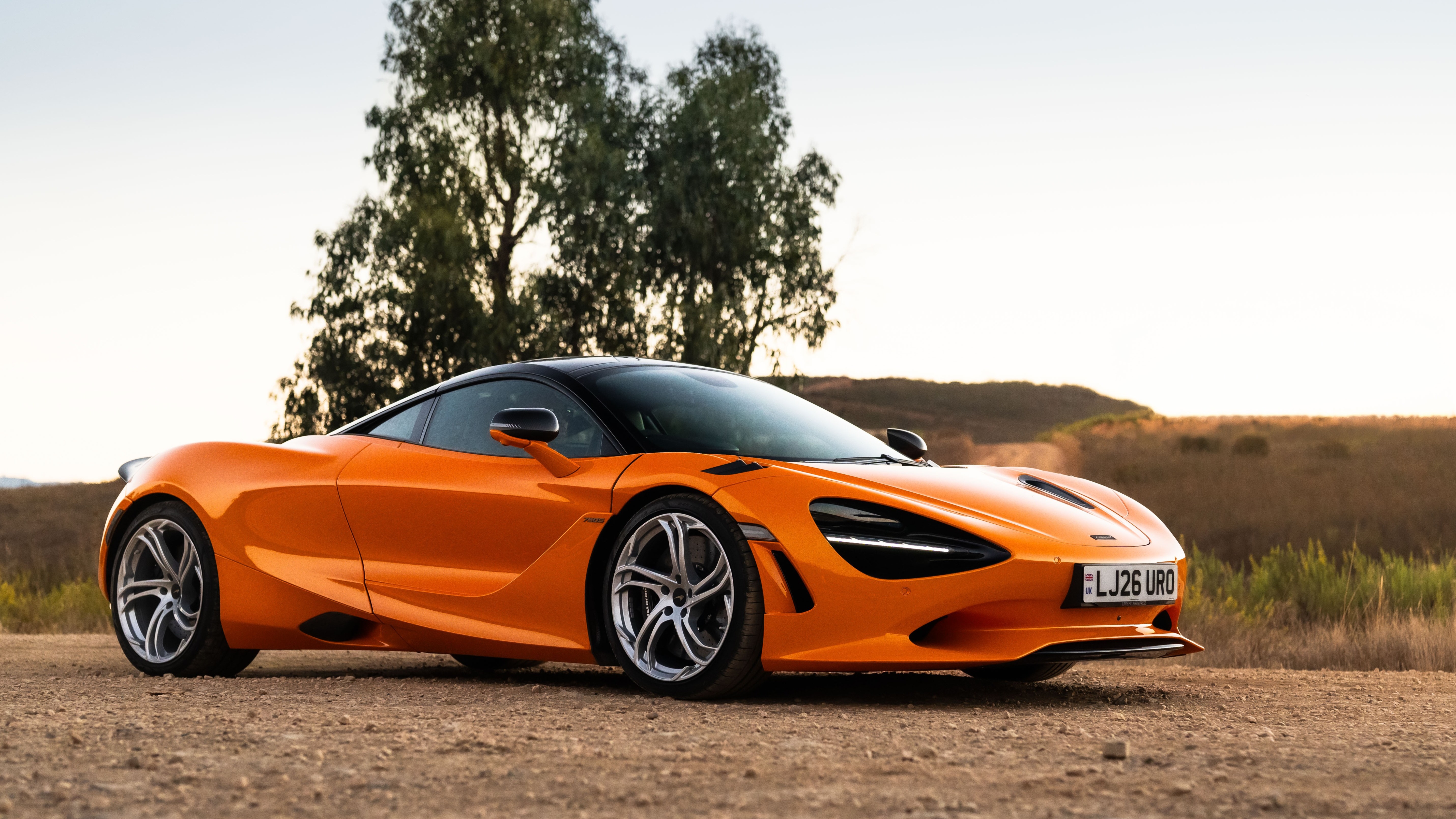 Orange McLaren 750S coupe parked on a gravel road, front three-quarter view