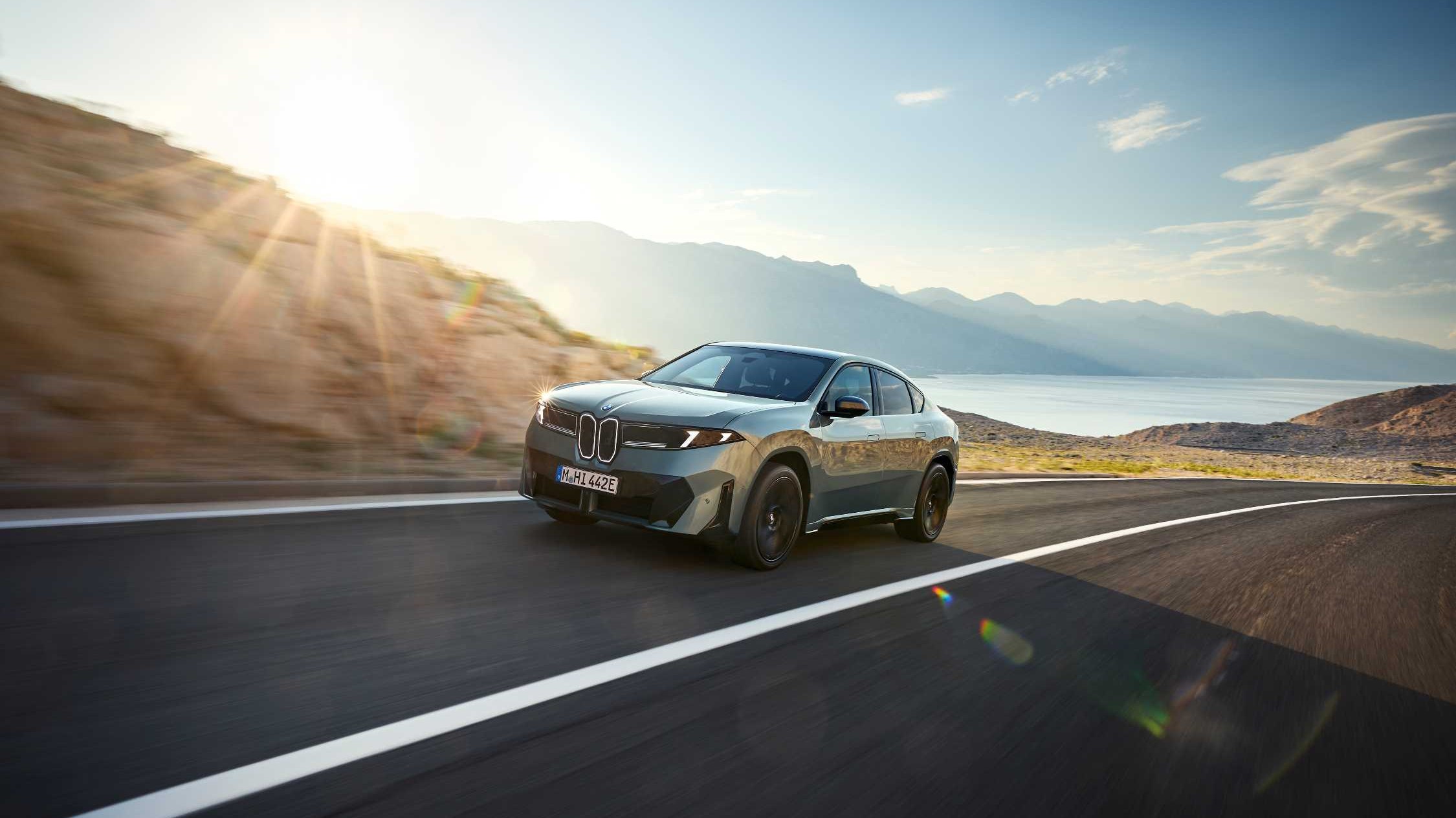 BMW iX4 electric coupe-SUV driving on a mountain road, front three-quarter view