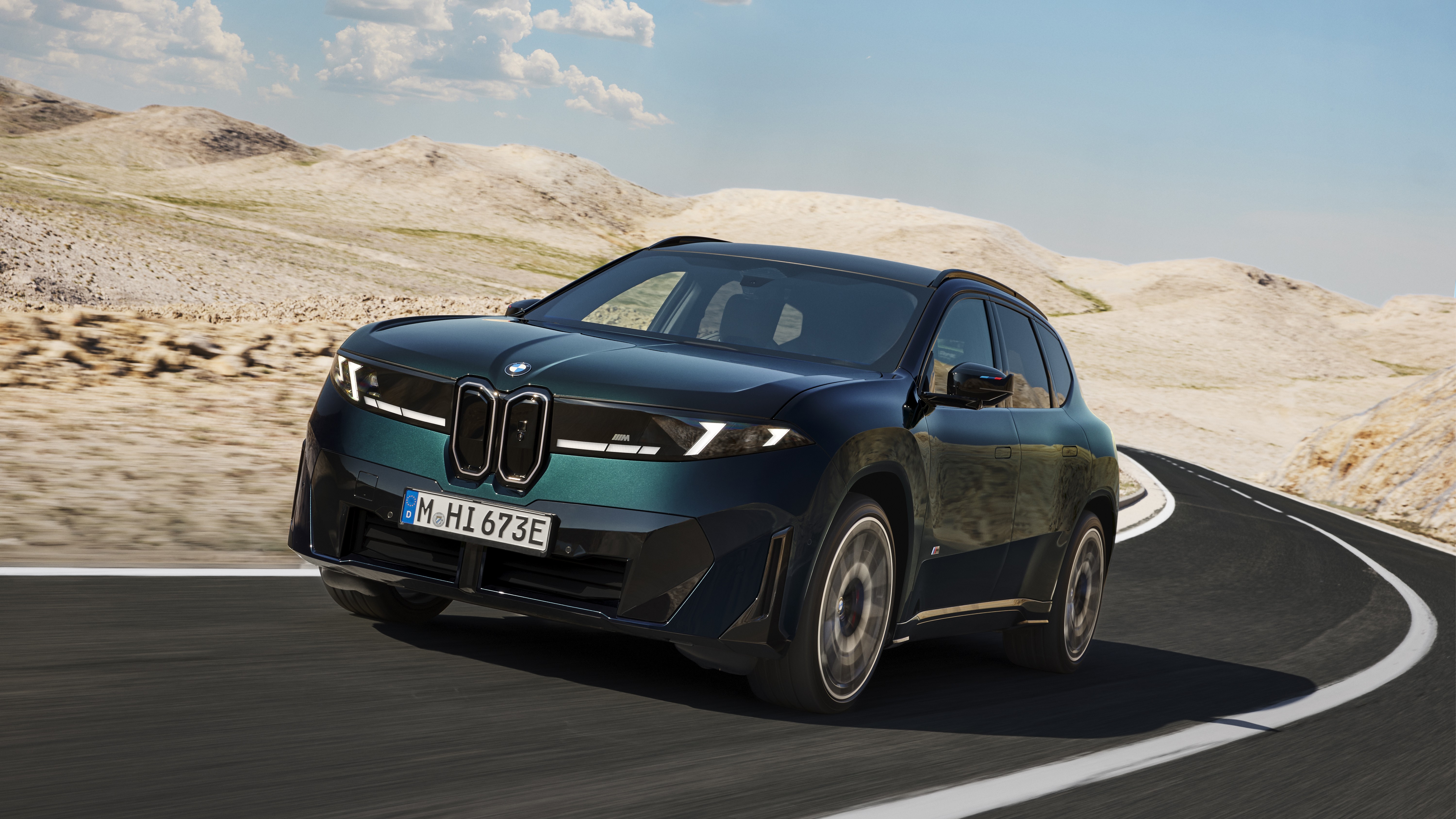 Dark green BMW iX3 M60 xDrive cornering on a desert road, front three-quarter view