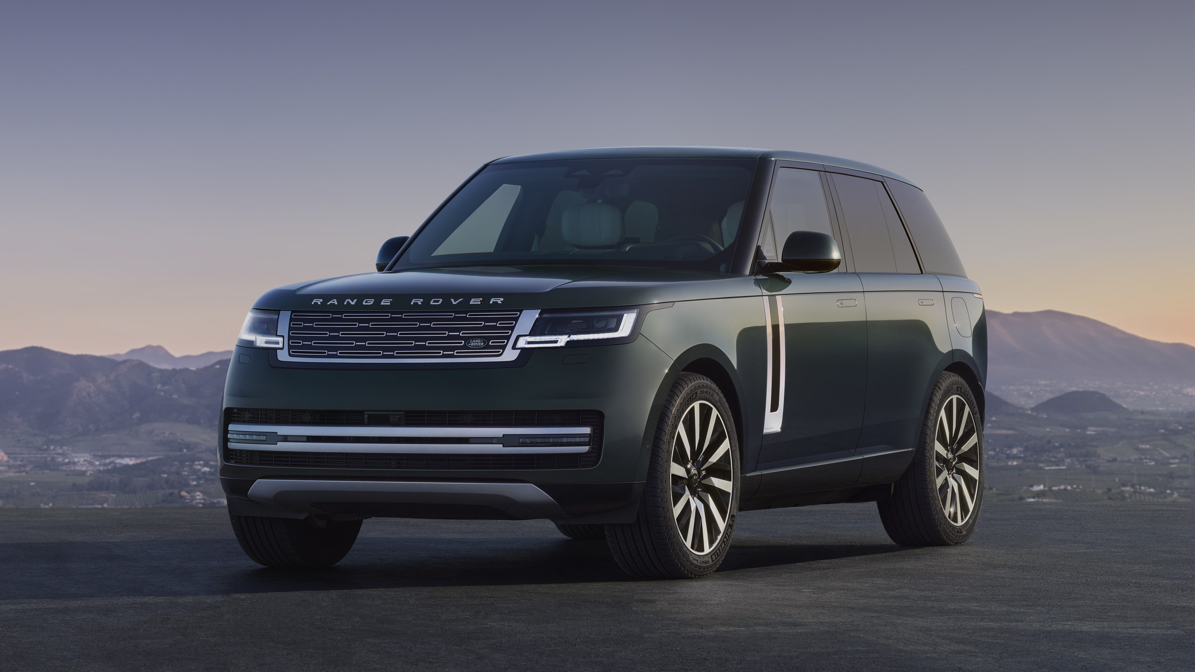 Green Range Rover luxury SUV, front three-quarter view at dusk