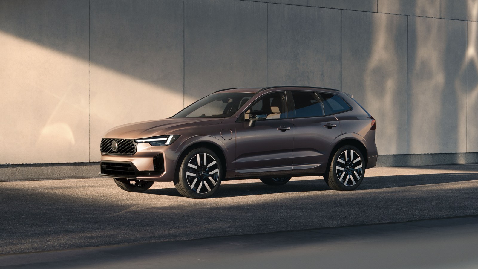 Bronze Volvo XC60 parked beside a concrete wall in low sunlight