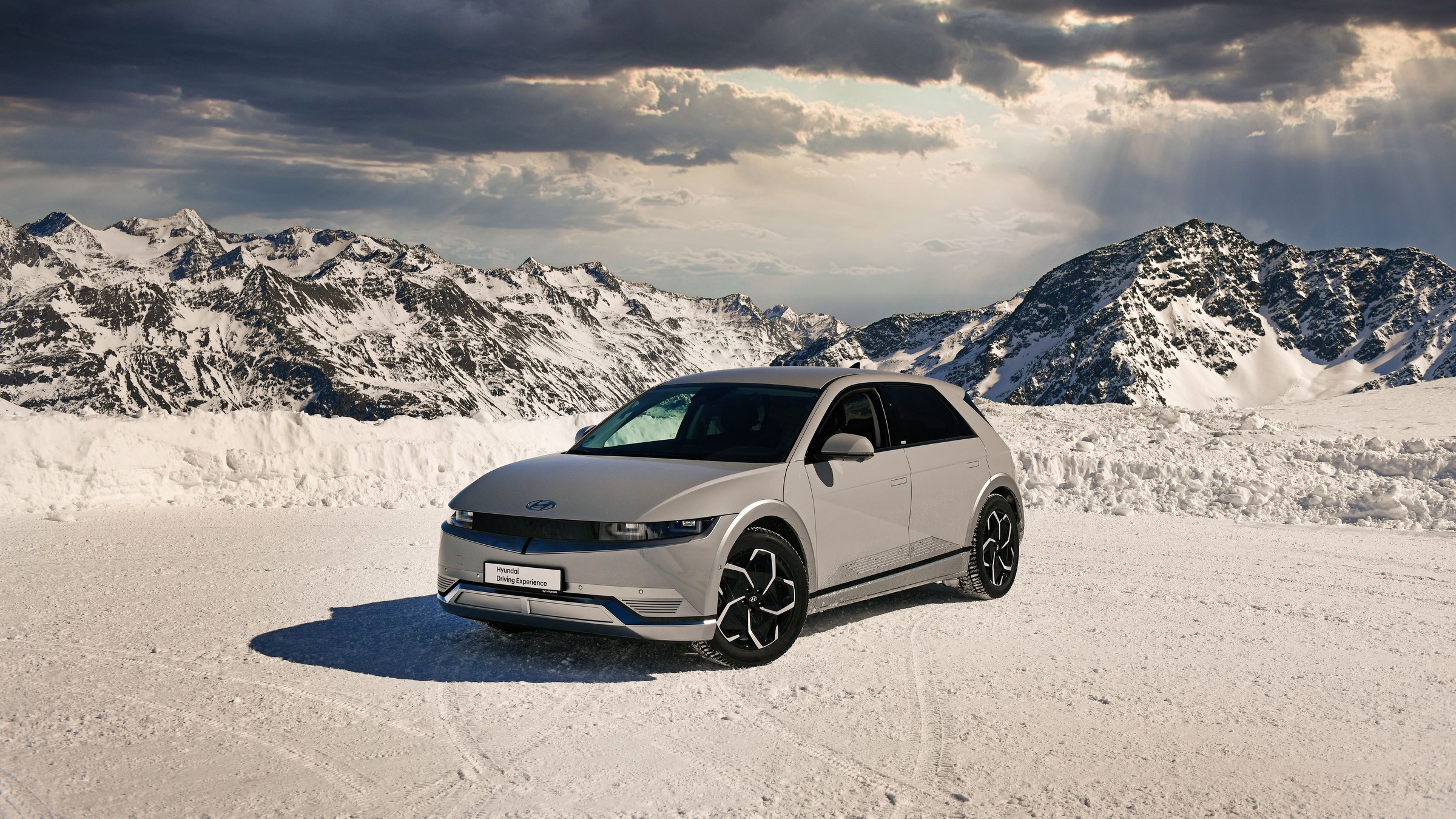 Silver Hyundai Ioniq 5 parked on packed snow below mountain peaks
