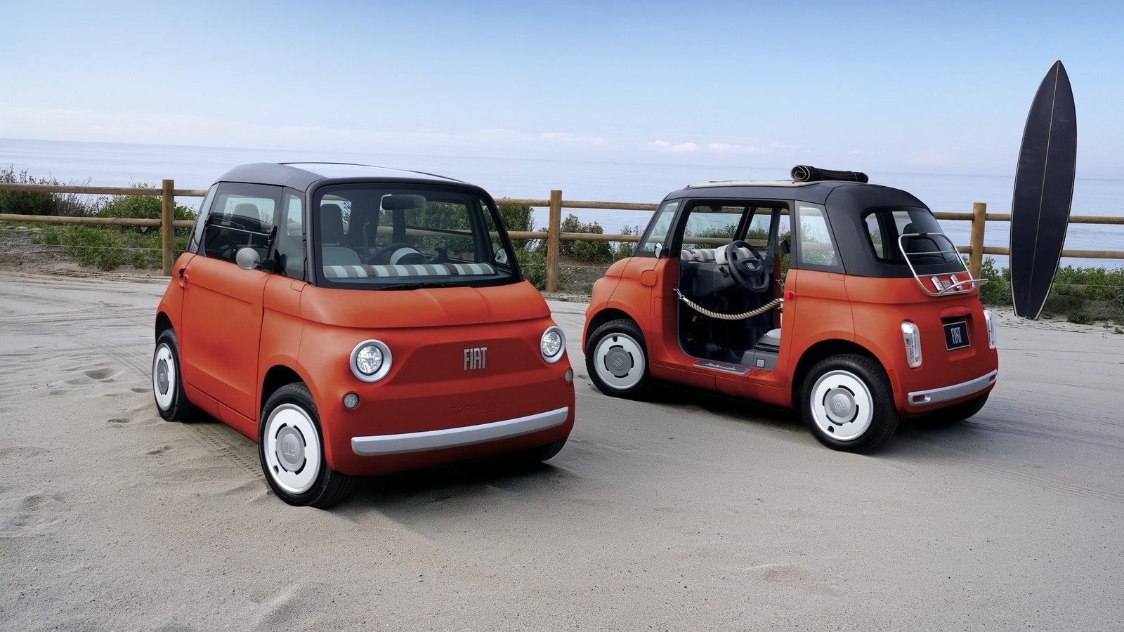 Two orange Fiat Topolino microcars parked on a beach