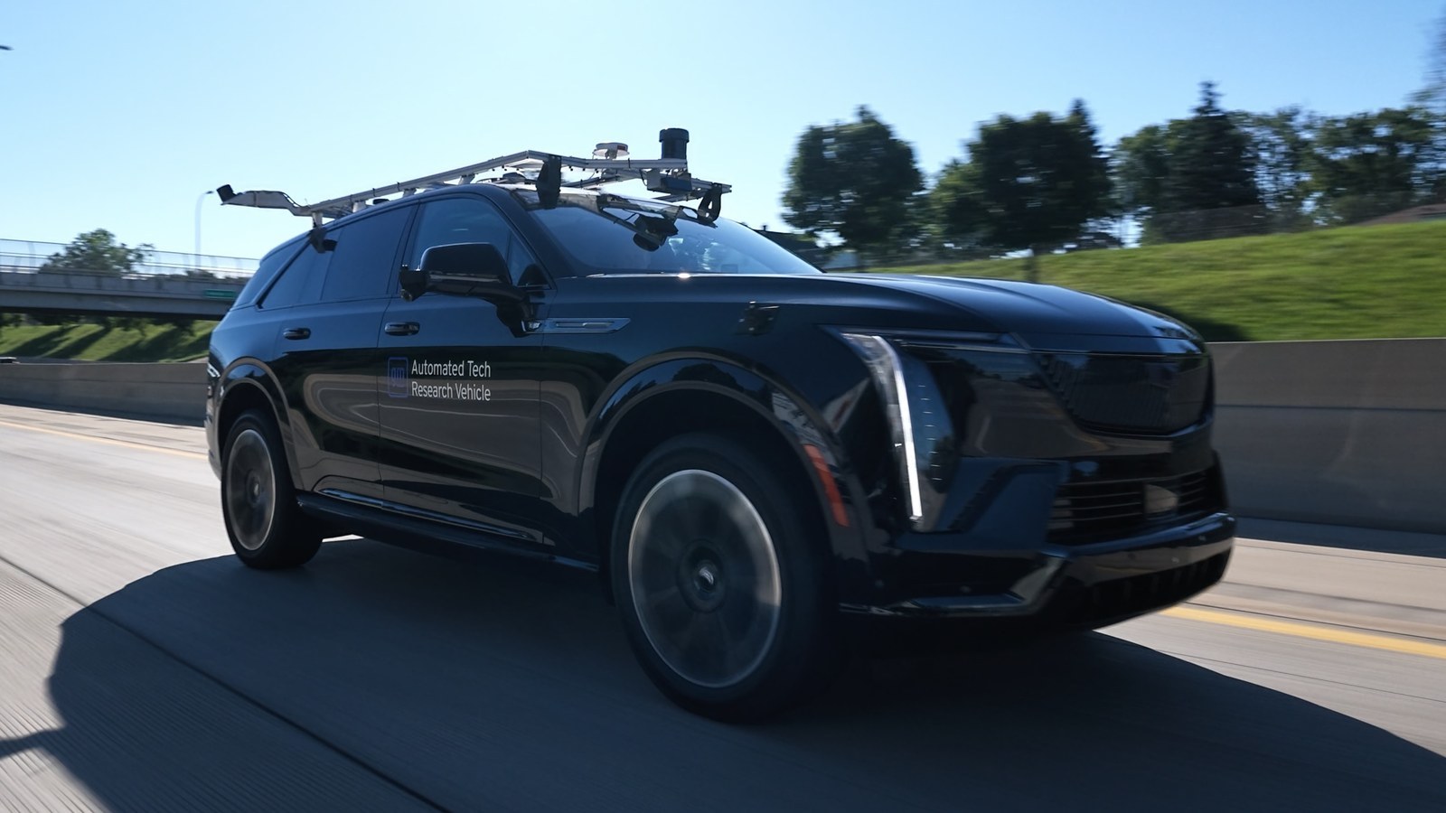 Black Cadillac SUV research vehicle with roof-mounted sensors on a highway