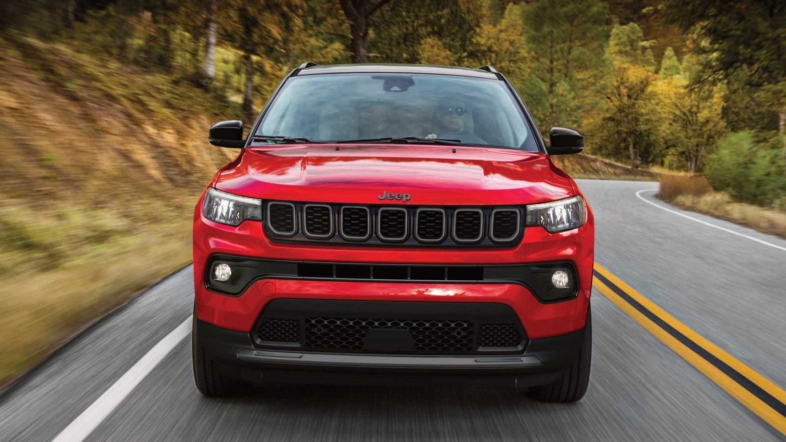 Red 2027 Jeep Compass Limited Altitude driving on a tree-lined road