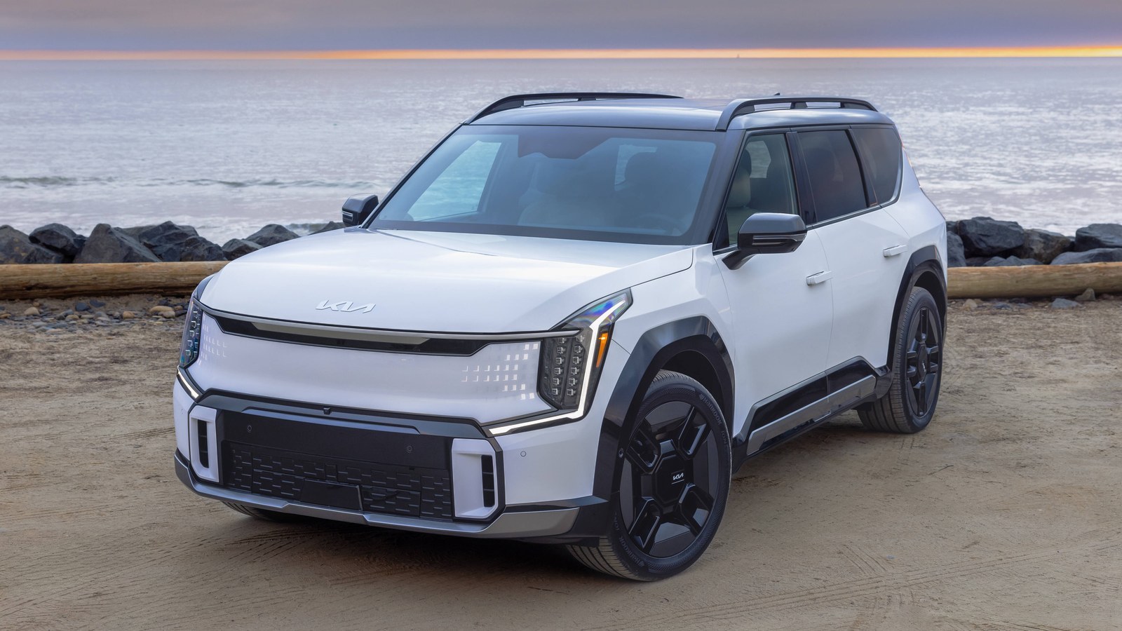 White 2027 Kia EV9 parked on a beach at sunrise