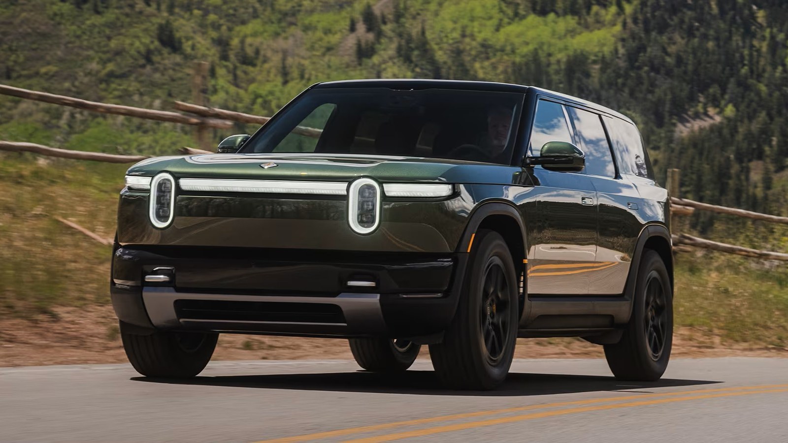 Green Rivian R2 driving on a mountain road, front three-quarter view