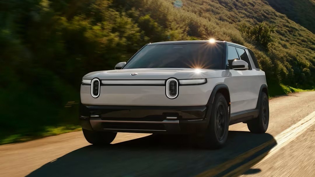 White Rivian R2 driving on a coastal hillside road