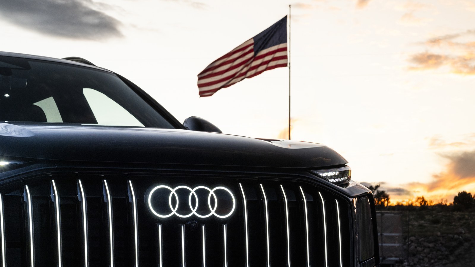 Illuminated Audi rings on an SUV grille with an American flag behind