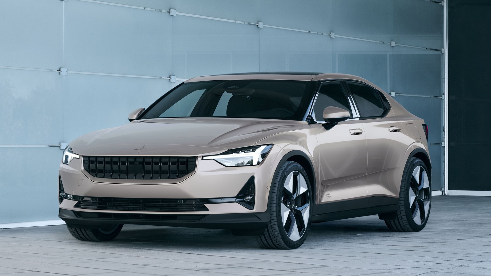 Beige Polestar 2 fastback parked in front of a glass garage door