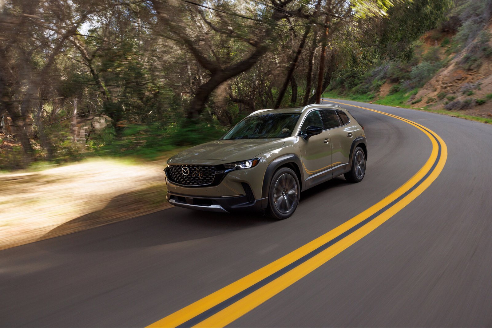 2026 Mazda CX-50 in Zircon Sand driving on a winding forest road