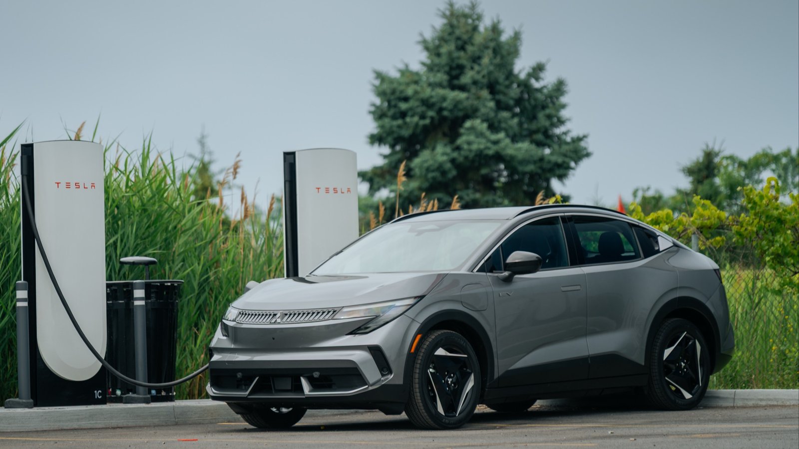 Gray 2027 Mitsubishi Eclipse Sportback EV plugged into a Tesla Supercharger