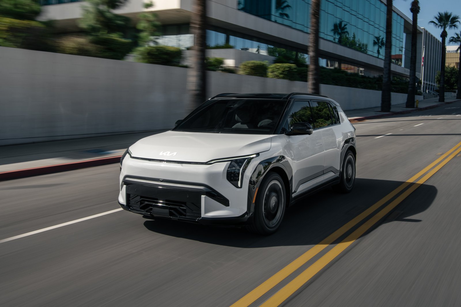 027 Kia EV3 driving on a city street, front three-quarter view
