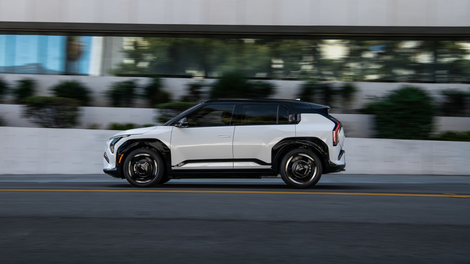 2027 Kia EV3 side profile driving past a modern office building