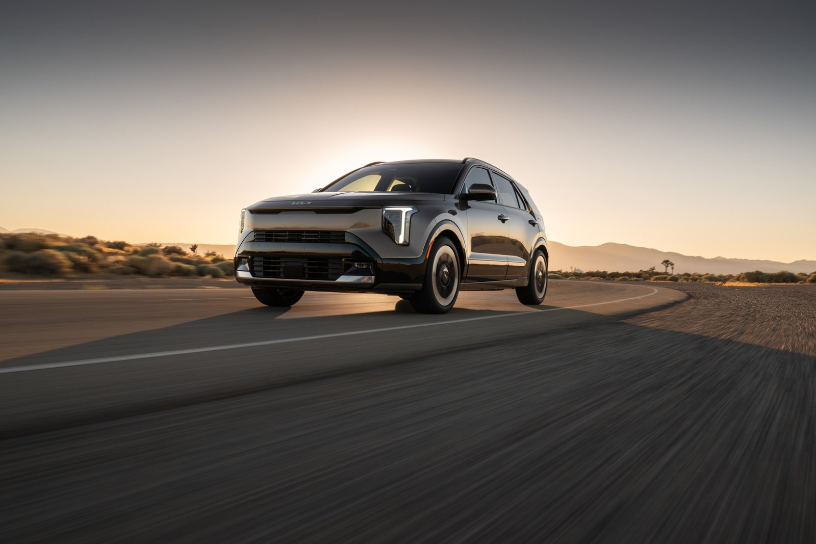 2027 Kia Niro driving on a desert road at dusk, front three-quarter view