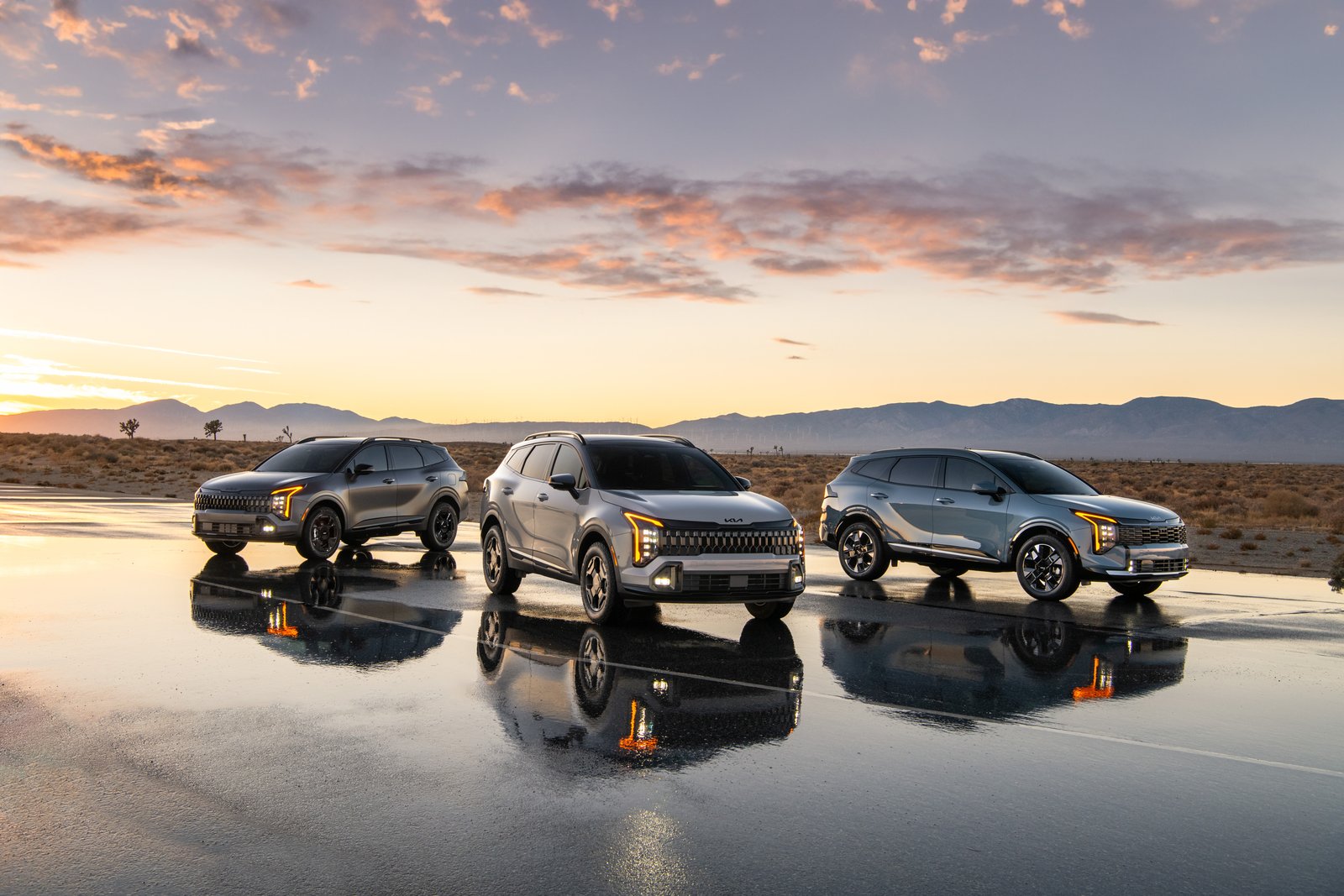 Three 2027 Kia Sportage variants lined up on wet pavement at dusk
