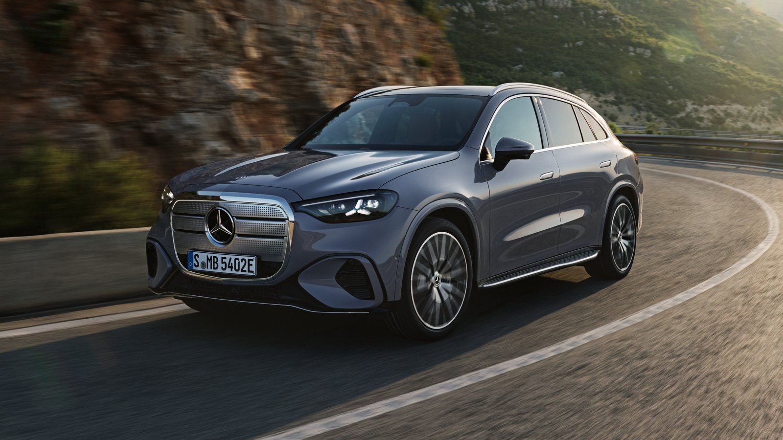 Silver Mercedes GLC 400 4MATIC Electric with chrome grille driving through a mountain curve