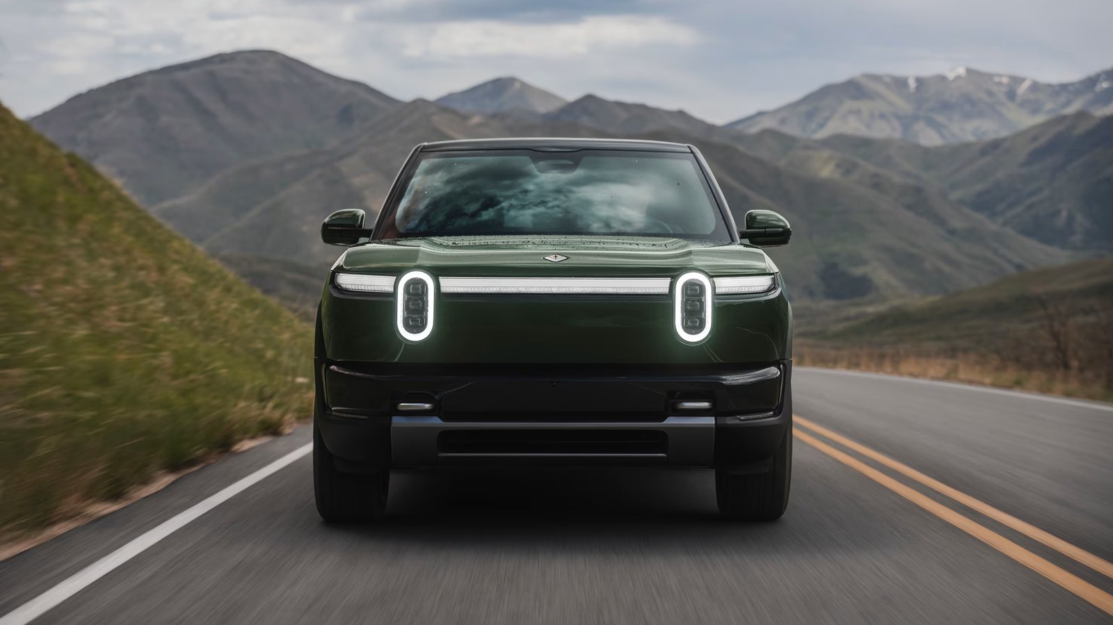 Rivian R2 in Forest Green driving on a mountain road, front view
