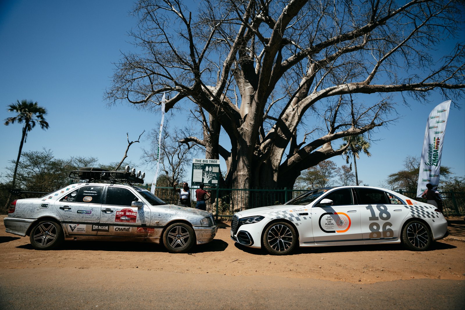 New Mercedes S-Class parked with signature-covered classic Mercedes under baobab tree