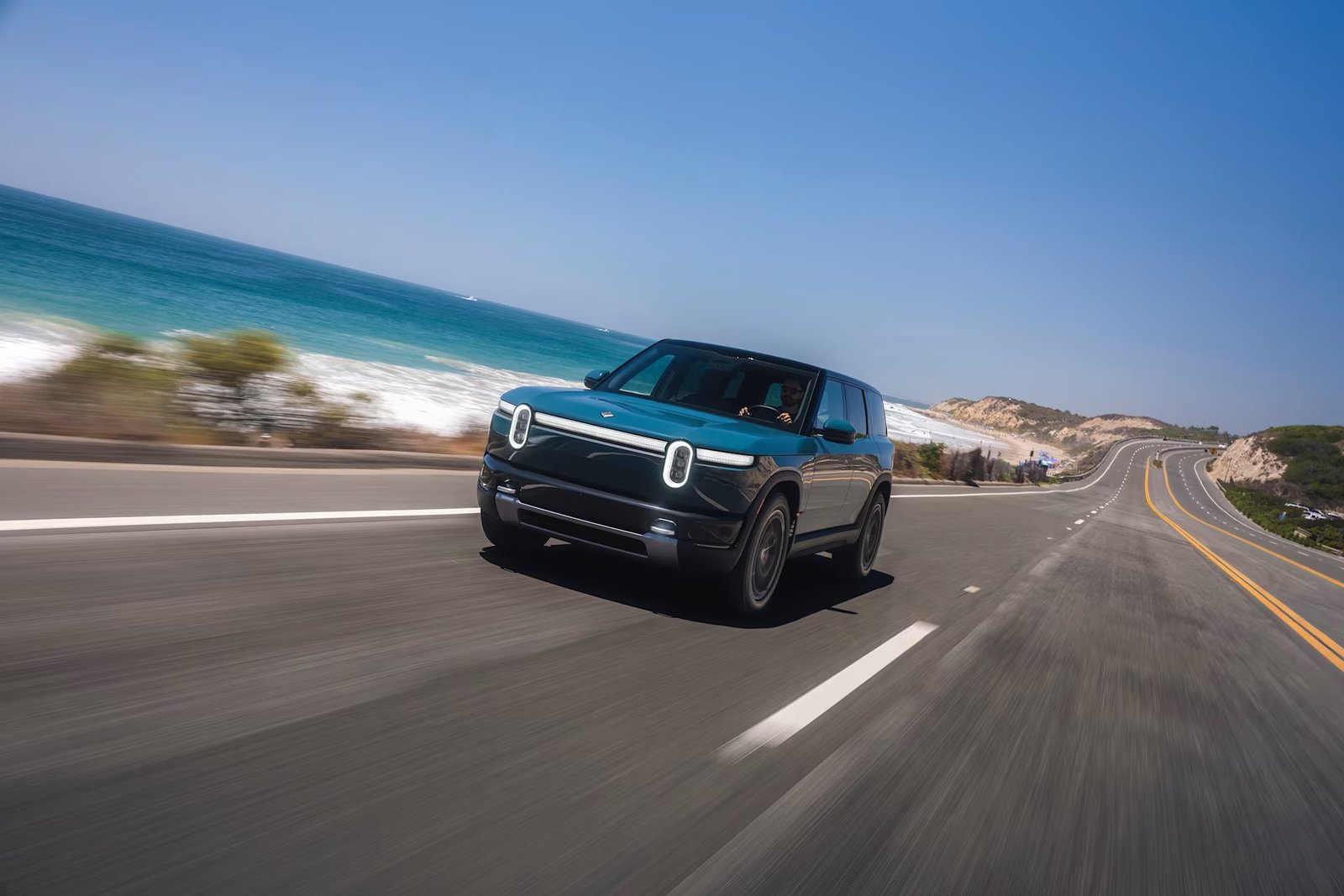 A first for the R2». Alt: "Rivian R2 driving on a coastal highway