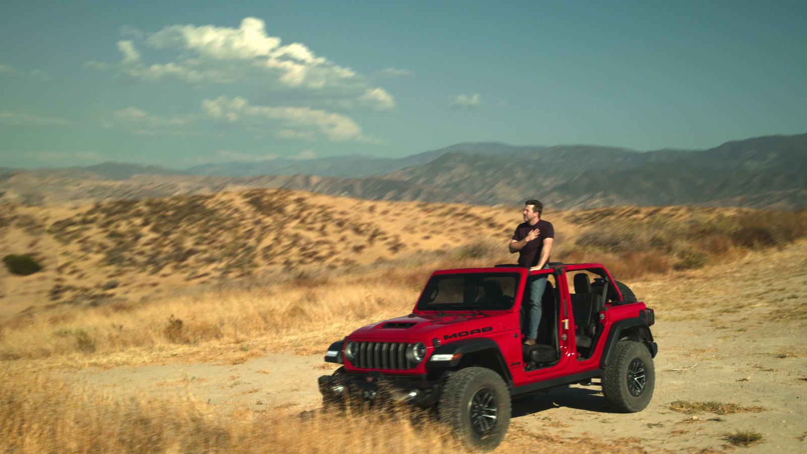 Jeep owner standing in doorless red Wrangler on hilltop