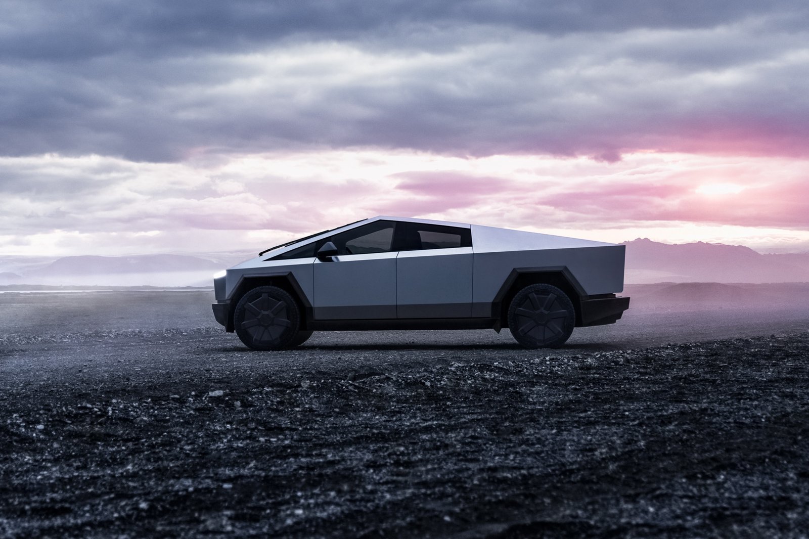 Tesla Cybertruck side profile on a dark gravel plain at sunset