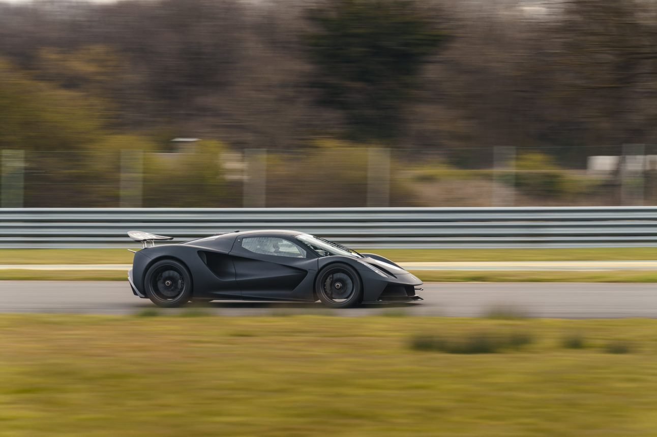 Matte black Lotus Evija at speed on a race track, side view