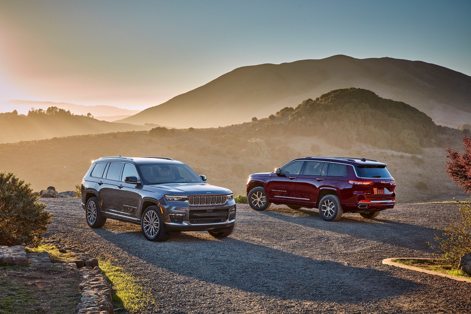Two Jeep Grand Cherokee L SUVs parked on a hilltop at sunset