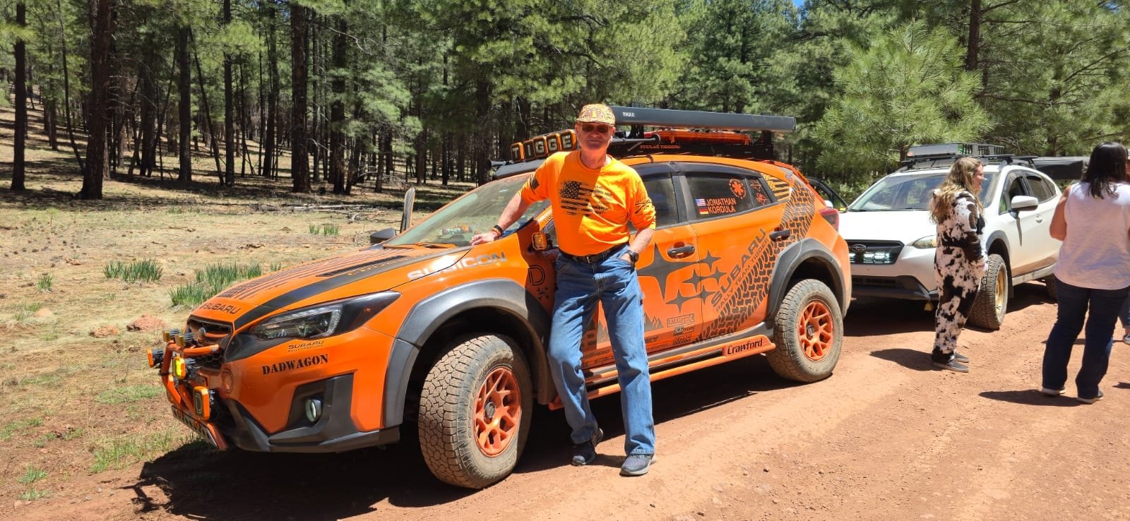 Modified orange Subaru Crosstrek with owner on a forest dirt road