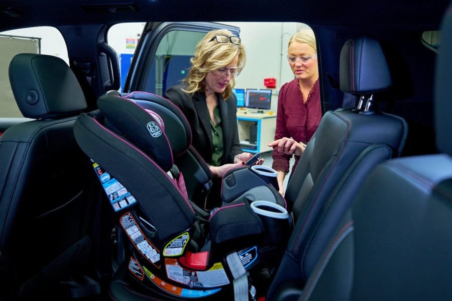 Two GM safety specialists inspecting a child car seat inside a test vehicle