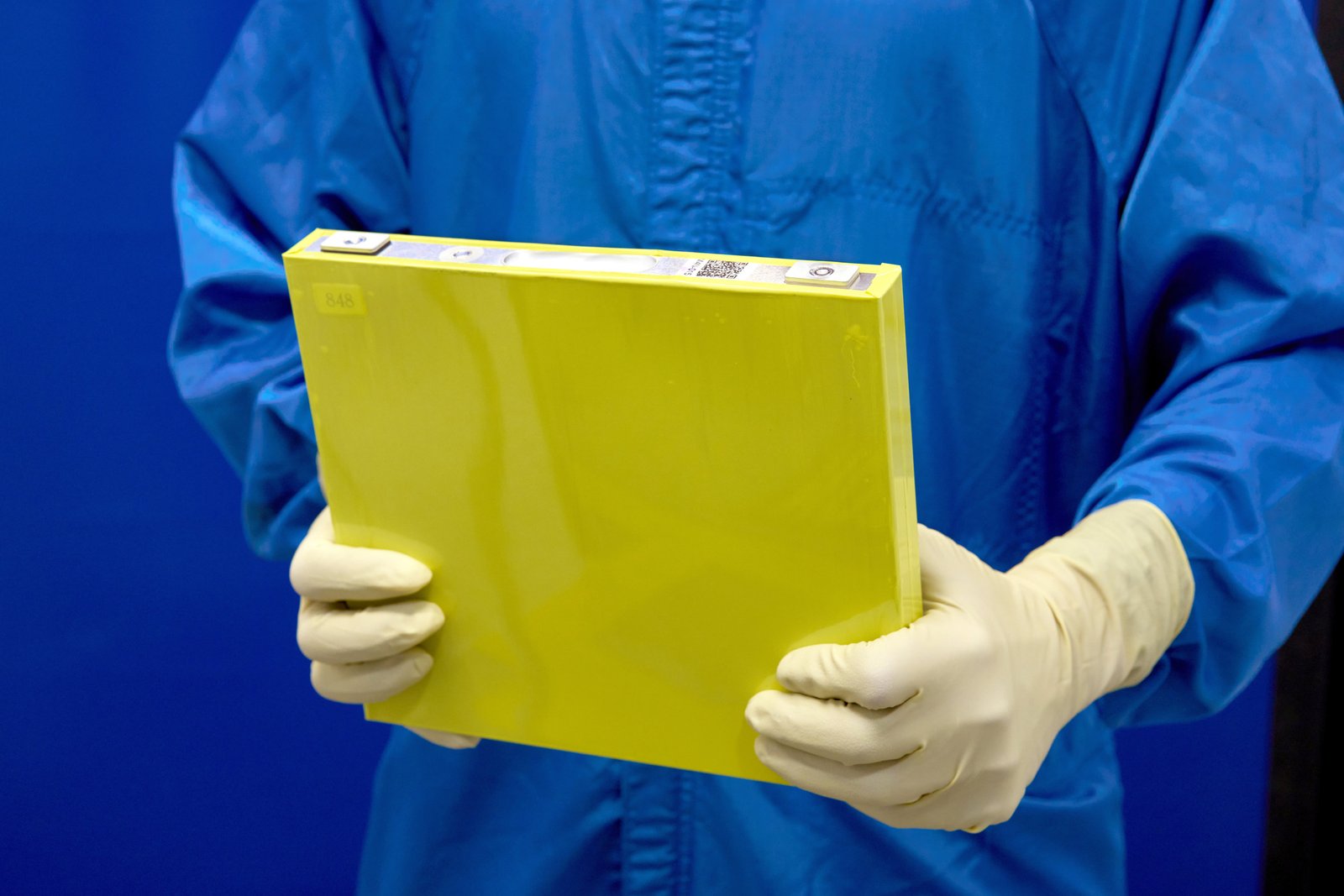 Technician in cleanroom gear holding a yellow GM LMR prismatic battery cell