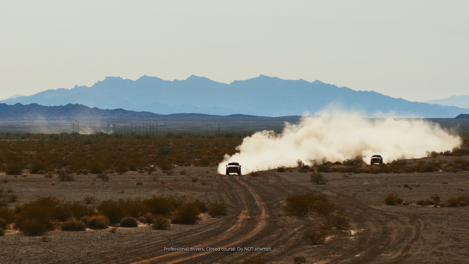 Two F-150 Raptor trucks kick up dust on a desert trail