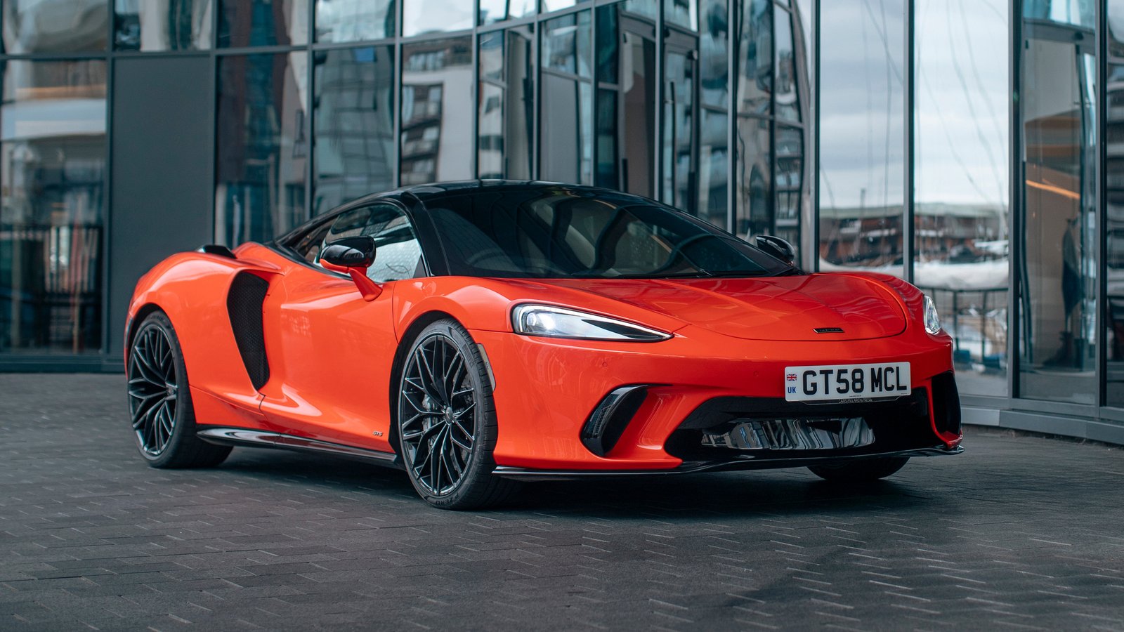 Orange McLaren GTS parked in front of a glass building